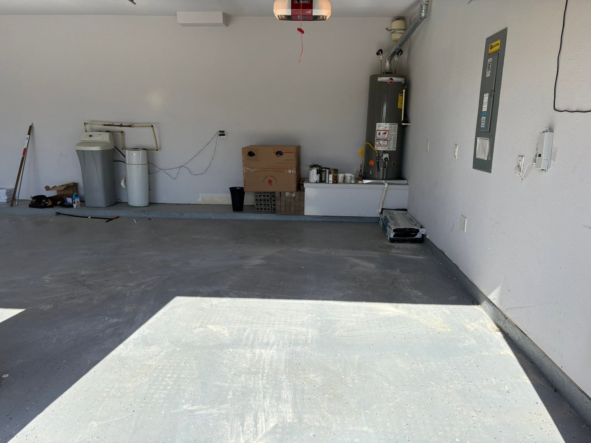 Empty garage interior with concrete floor, storage items along the back wall, and sunlight across the floor
