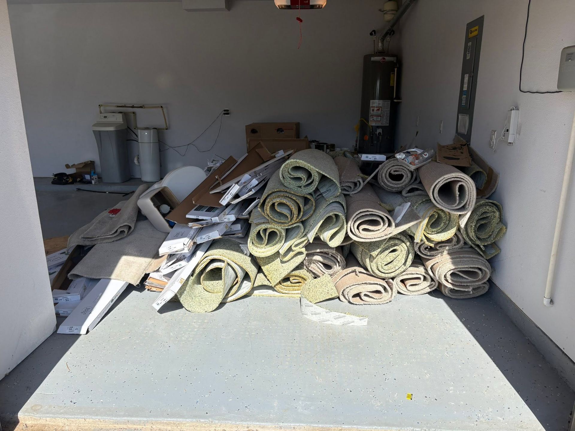 Stacked rolled rugs on a truck bed in a garage, with cardboard boxes and metal containers in the background.