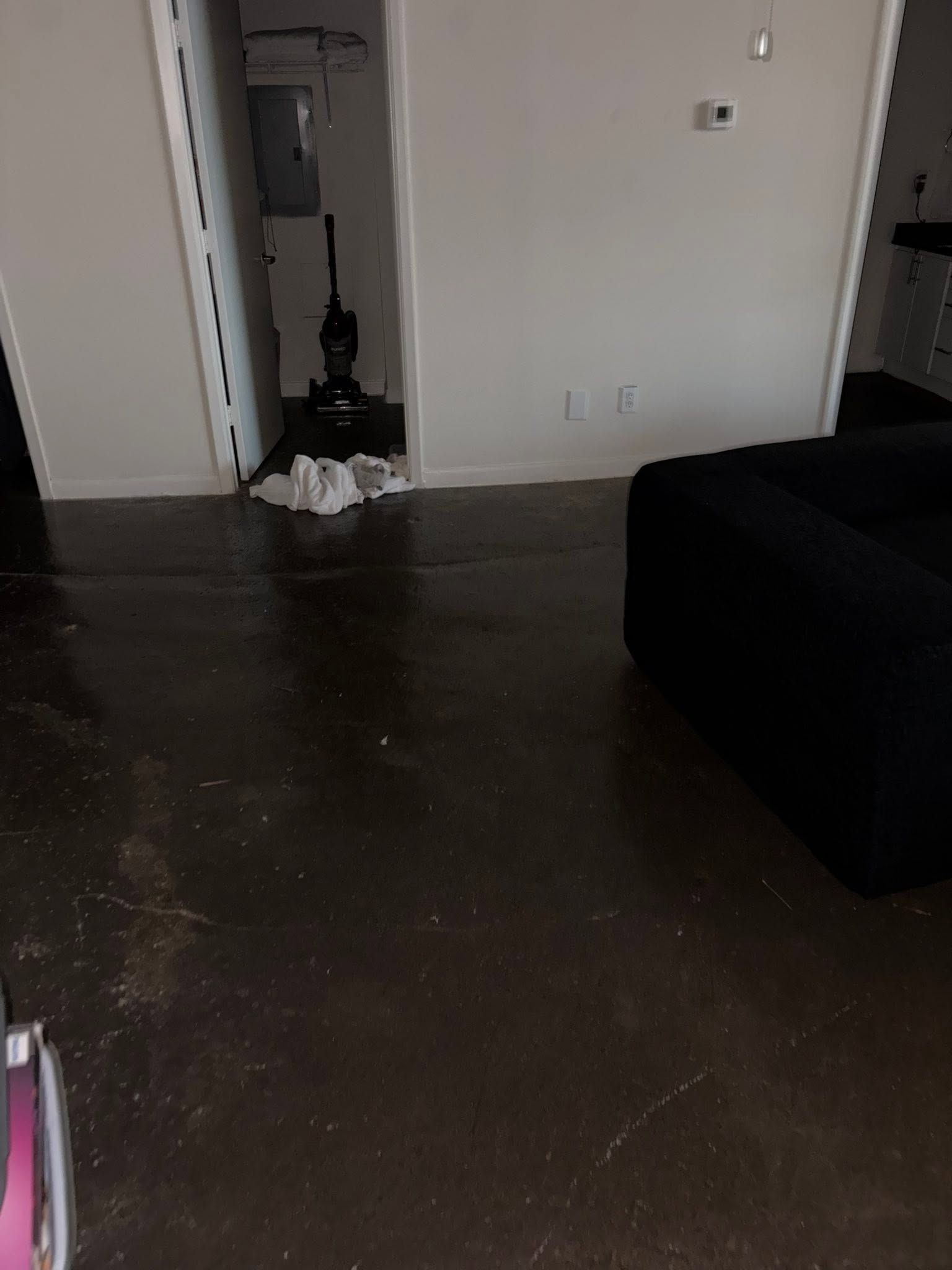 Dim living room with dark floor, open doorway, and black couch on the right.