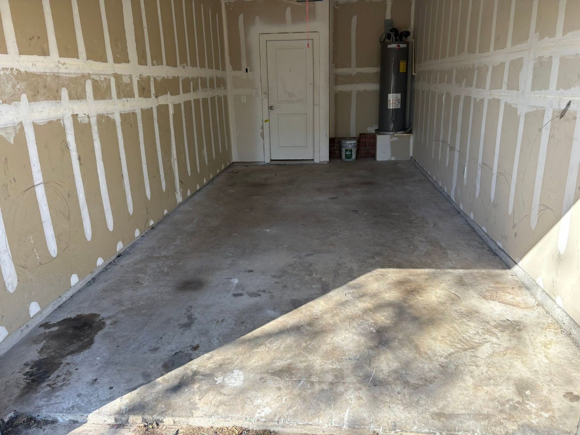 Empty garage interior with unfinished drywall, concrete floor, and sunlight near the opening