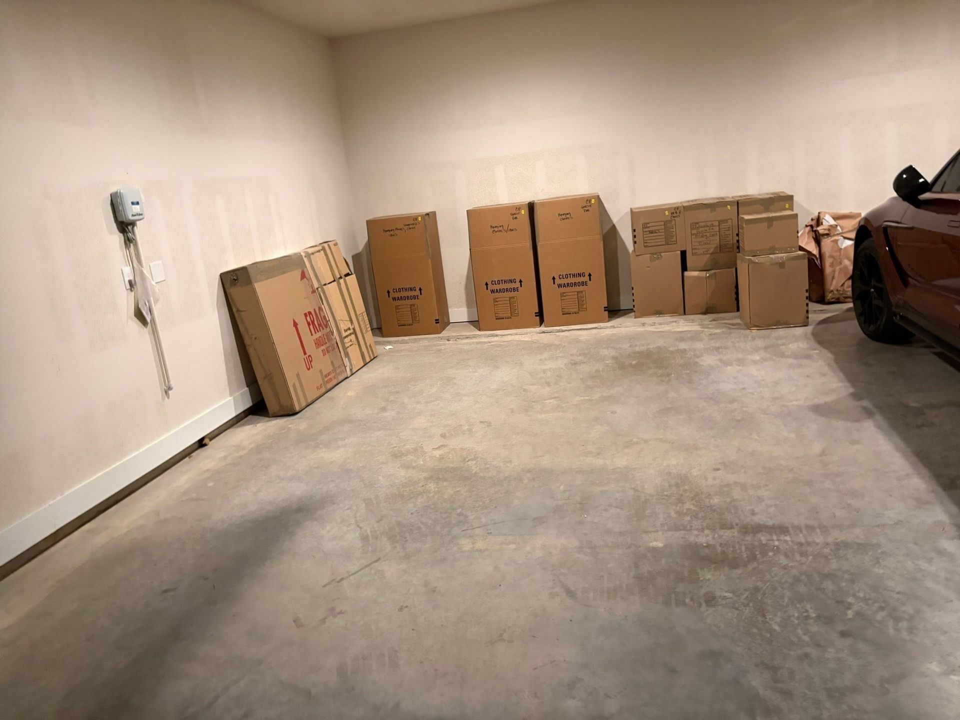 Empty garage with several cardboard moving boxes lined against the wall beside a parked car.