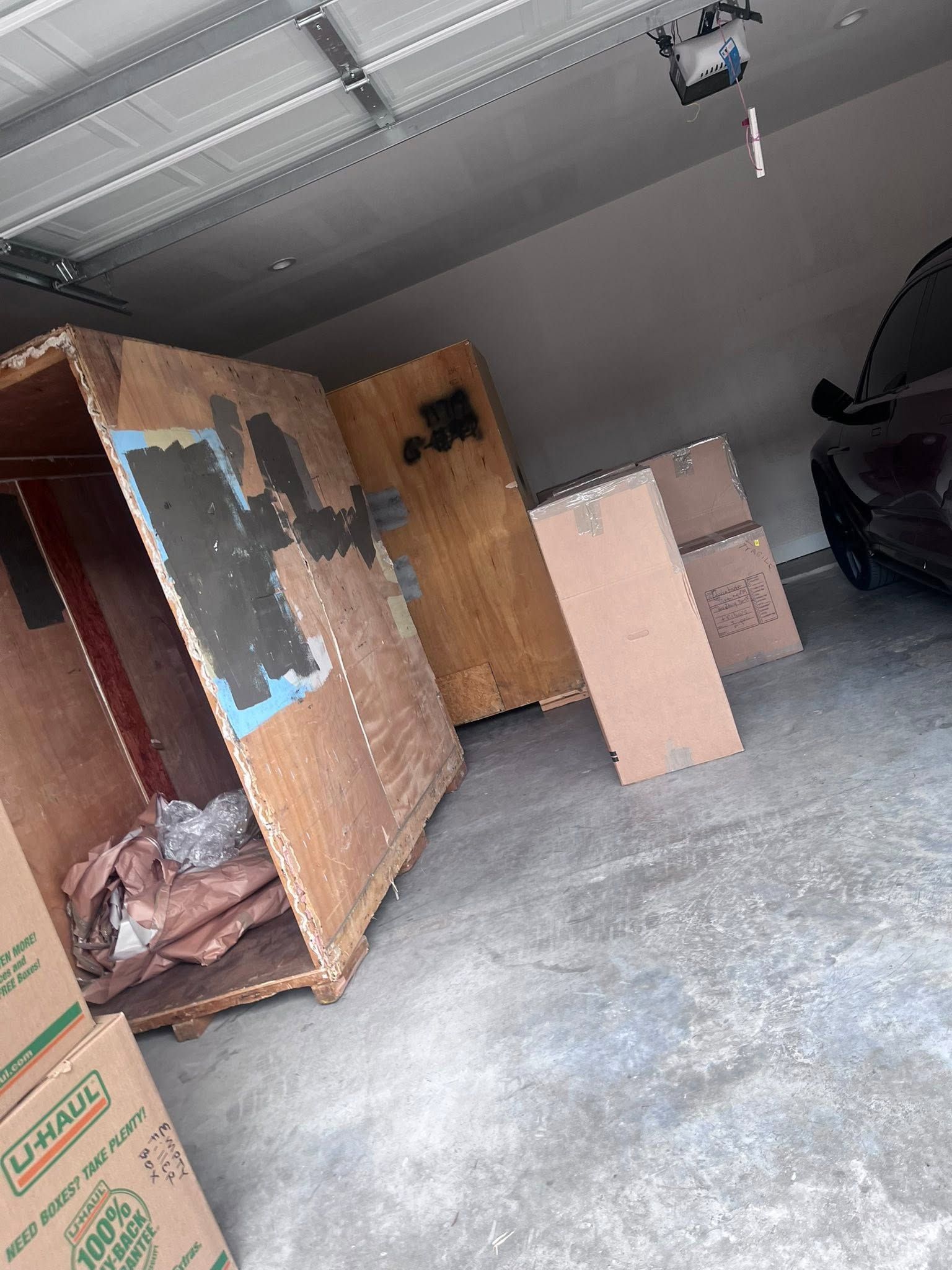 Garage with open cardboard boxes and large wooden panels near a parked car.