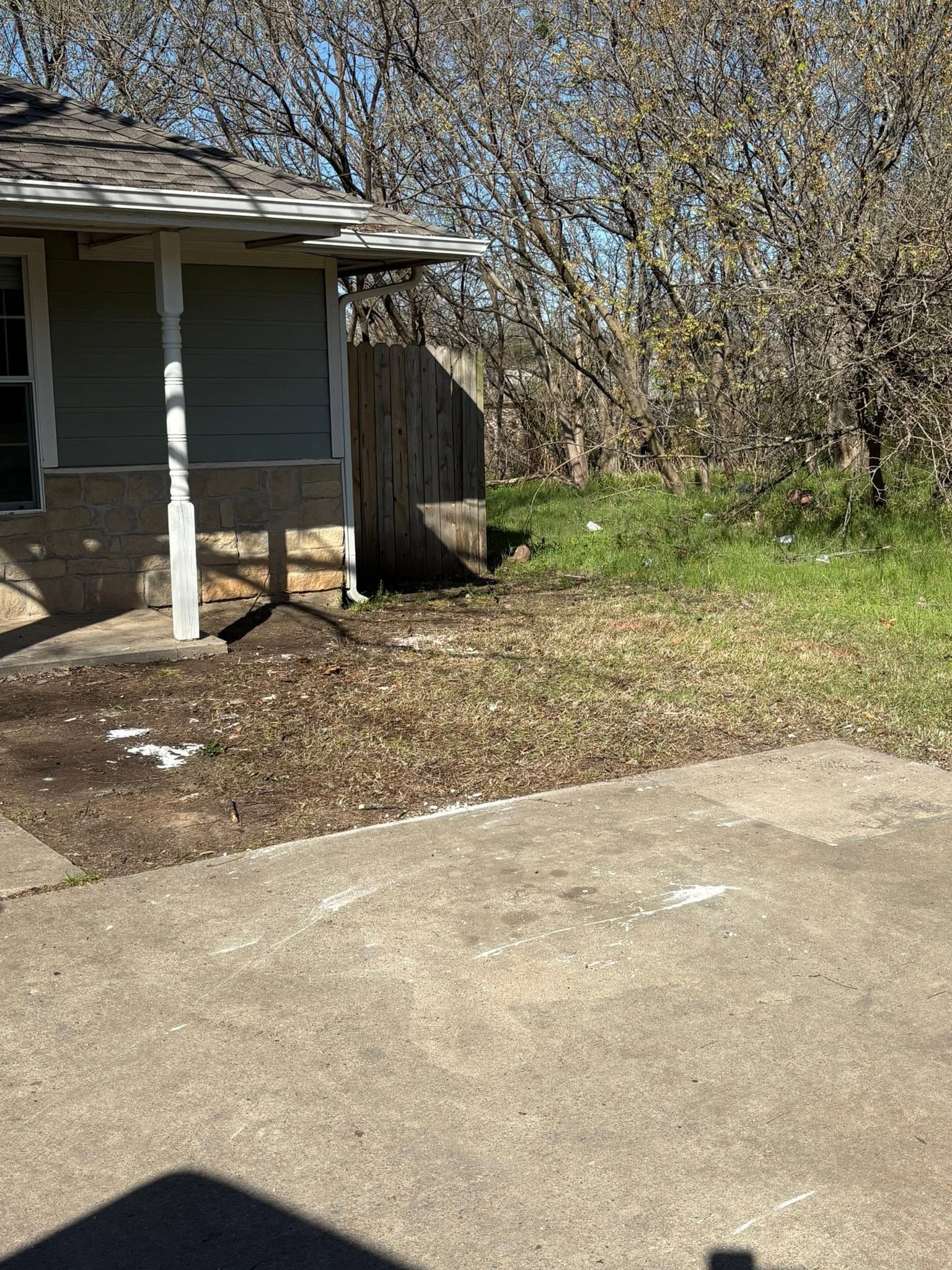 Old house porch beside a concrete driveway and leafless trees in a yard