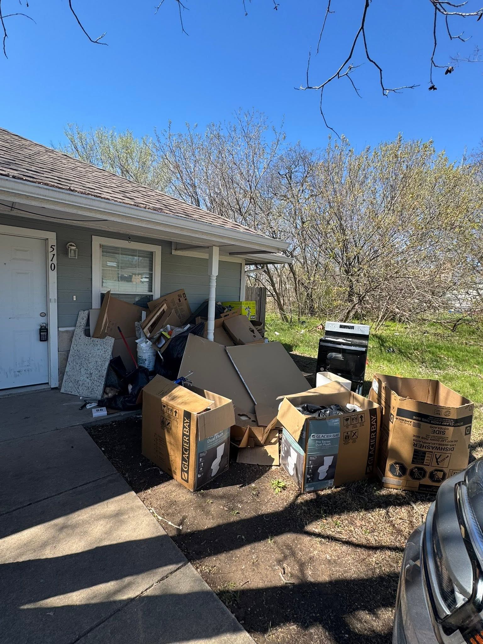 Pile of cardboard boxes and debris outside a house beside a driveway on a sunny day
