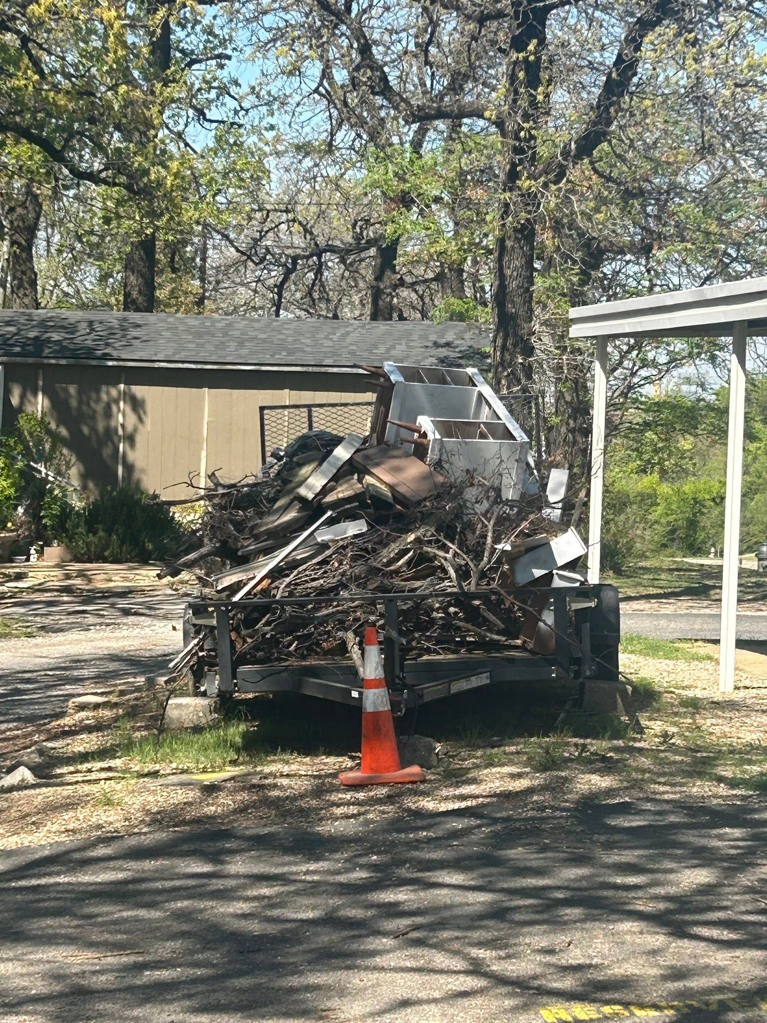 Truck carrying debris parked on a driveway, with an orange traffic cone in front and trees nearby