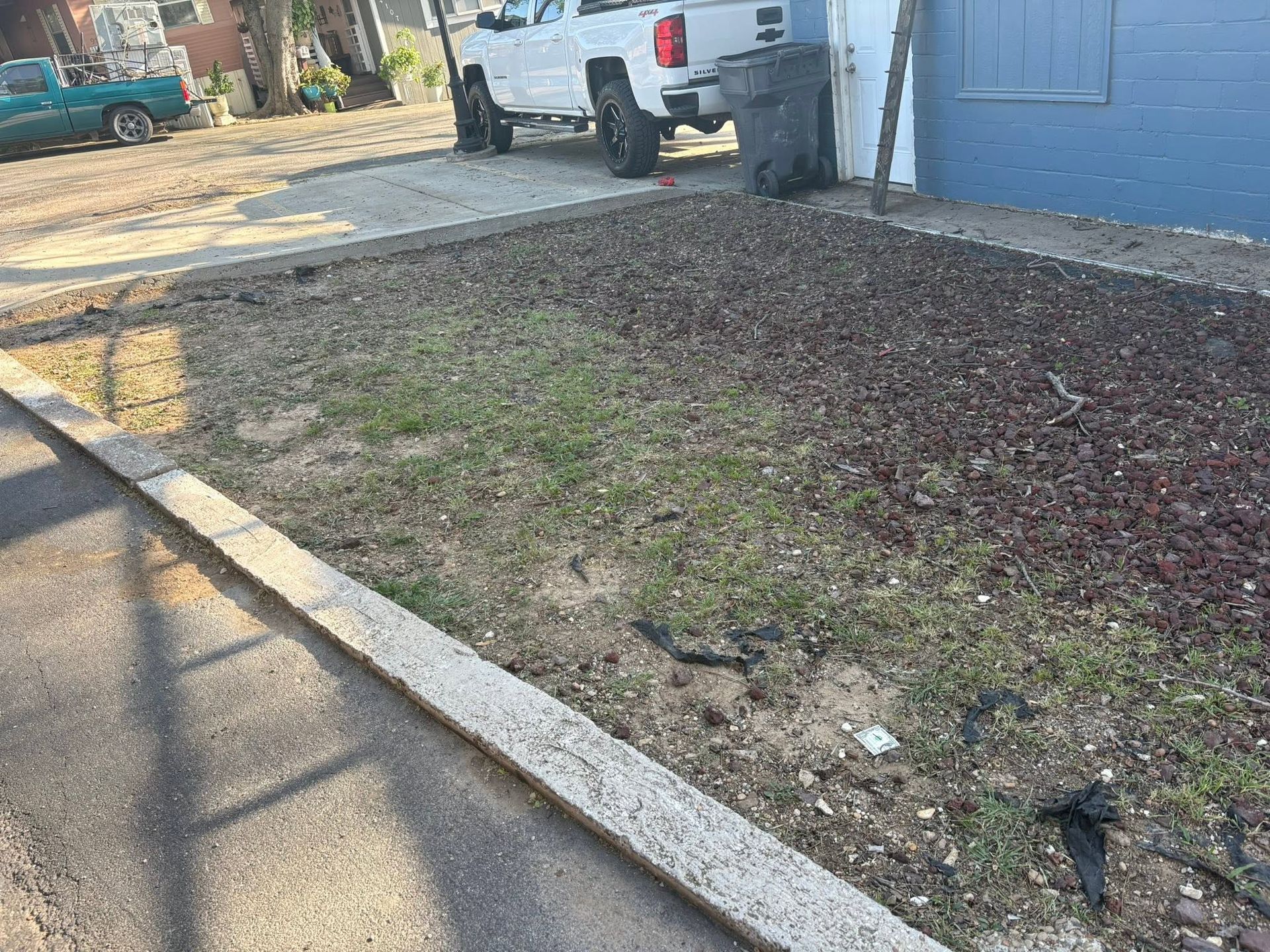 Front yard with patchy grass beside a driveway, parked white truck, and blue garage door.