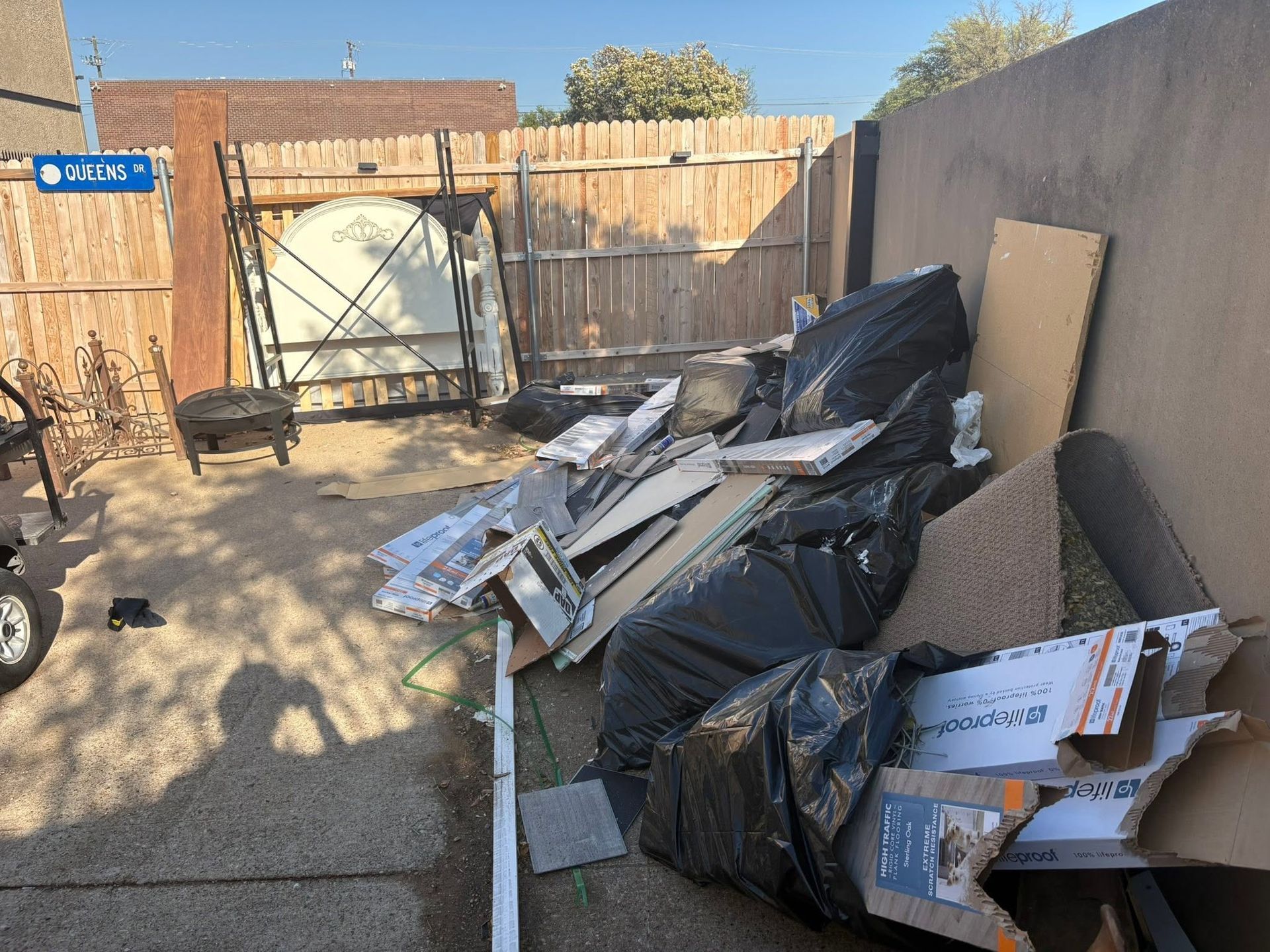 Backyard with piled construction debris, black trash bags, and scrap wood along a concrete wall