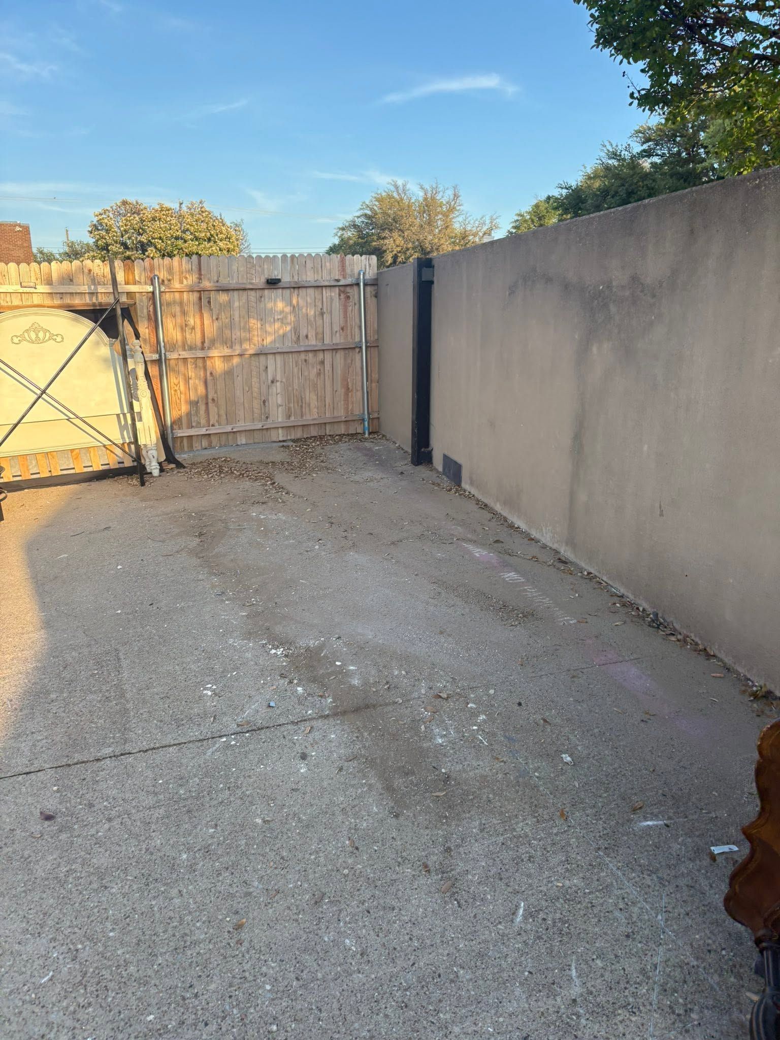 Gravel driveway and wooden gate beside a tall stucco wall in late-afternoon light