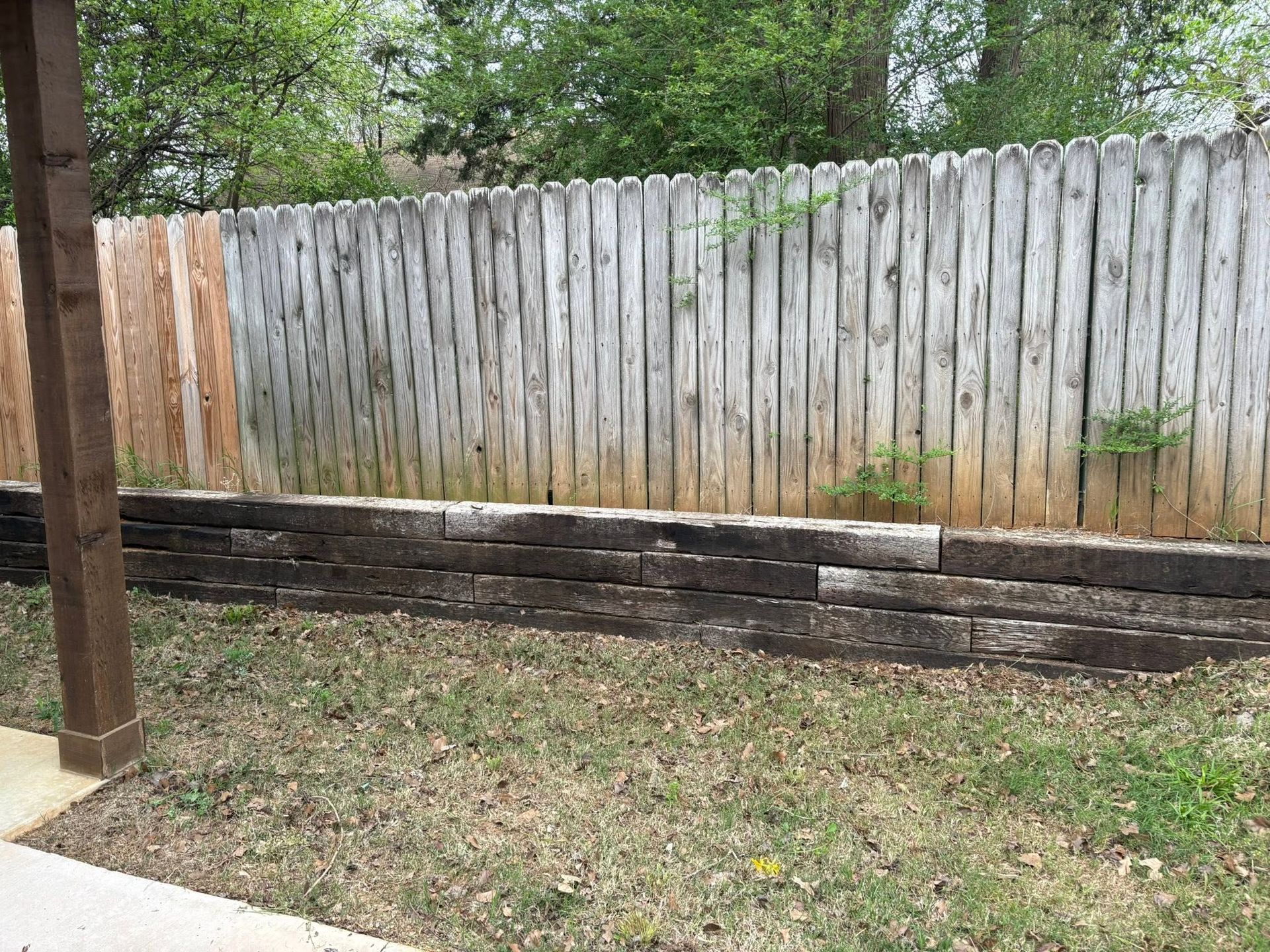 Backyard with grass, weathered wooden fence, and low stacked stone retaining wall