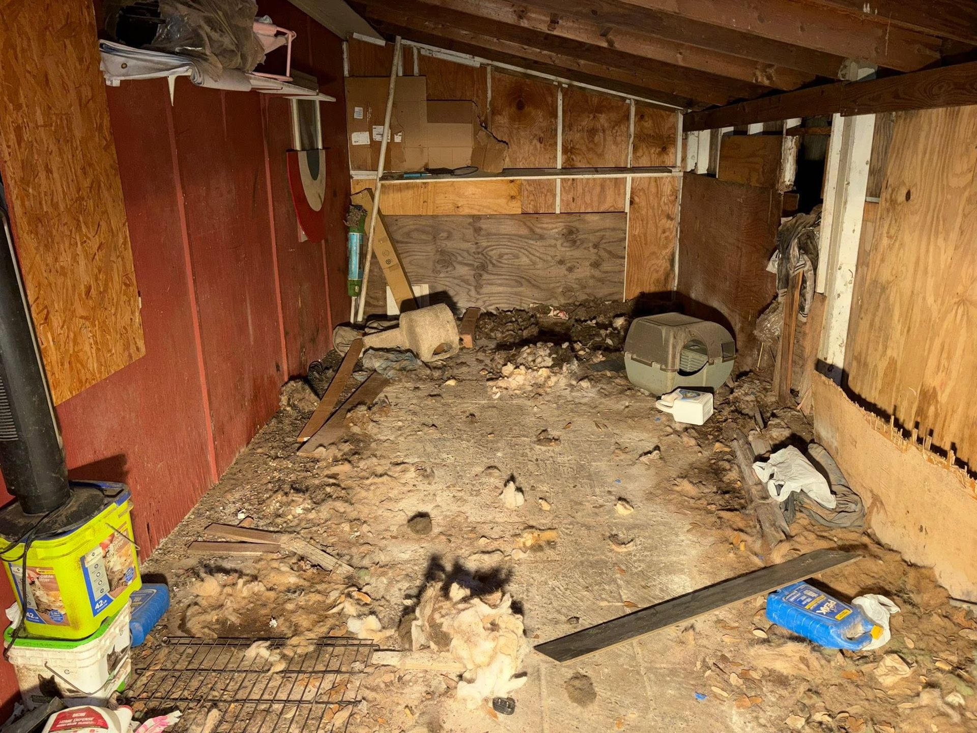 Cluttered crawl space with wood paneling, exposed beams, debris, and a yellow can in the corner