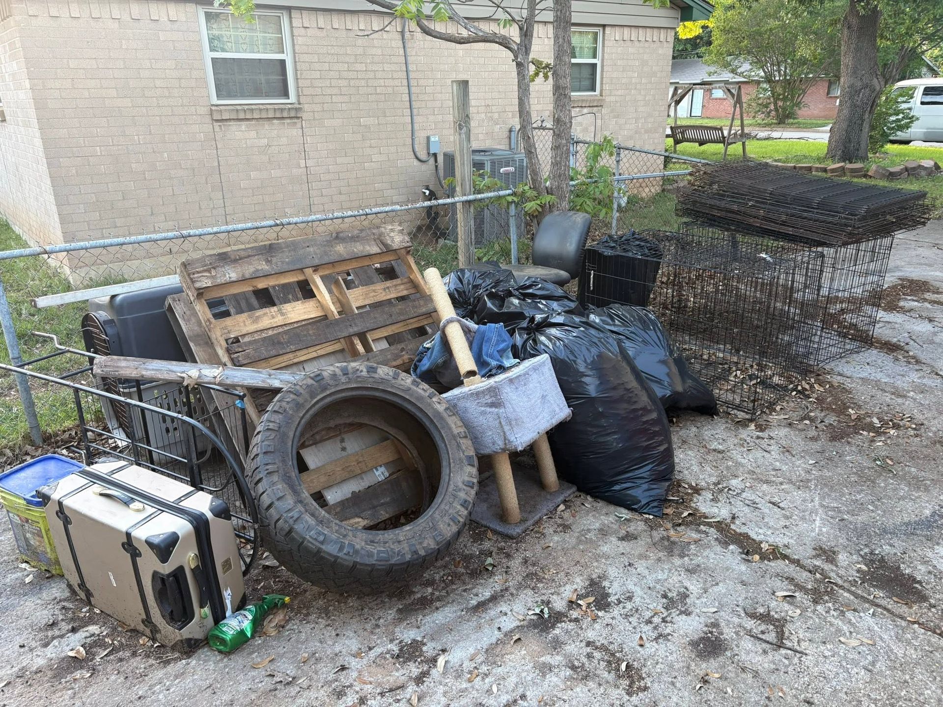 Junk pile of tires, pallets, bags, and furniture debris beside a brick building in a yard