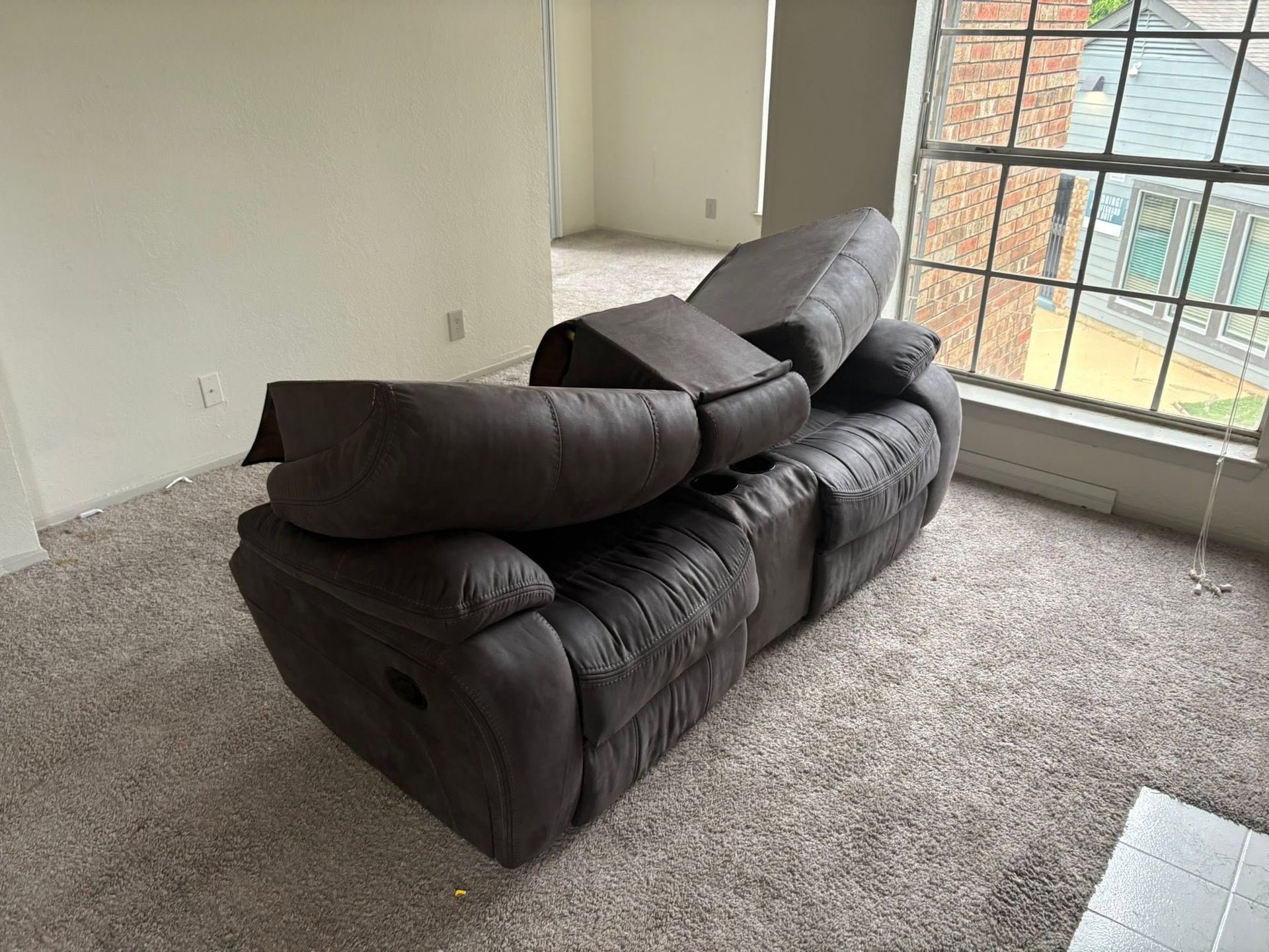 Dark gray sectional sofa in an empty carpeted room near a large window.