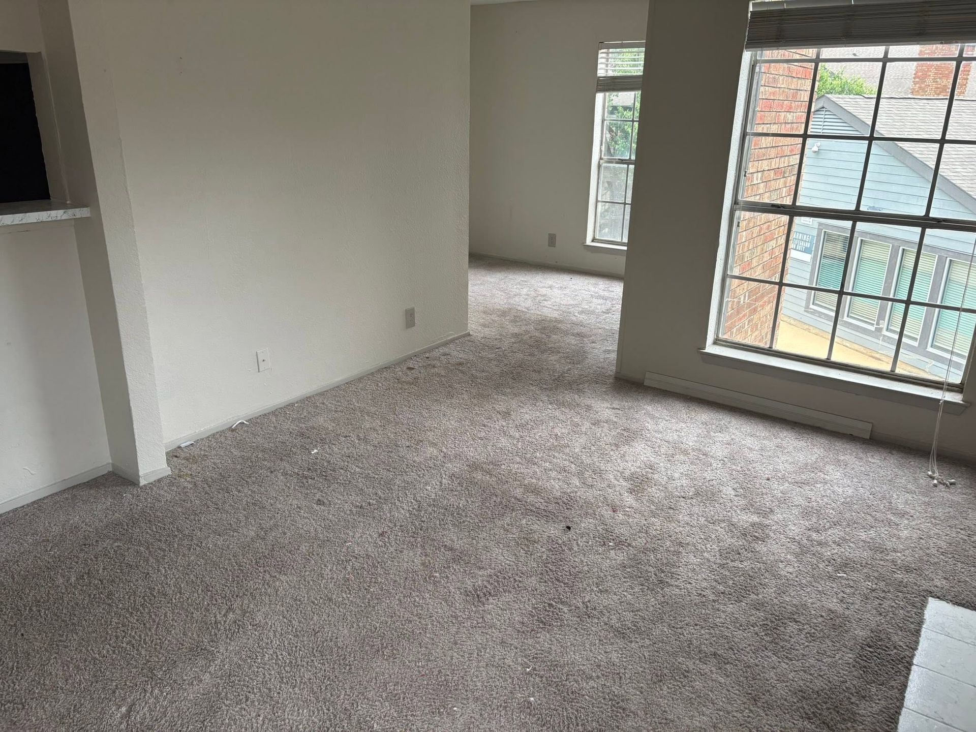 Empty carpeted room with white walls, a closet opening, and a large window letting in daylight.