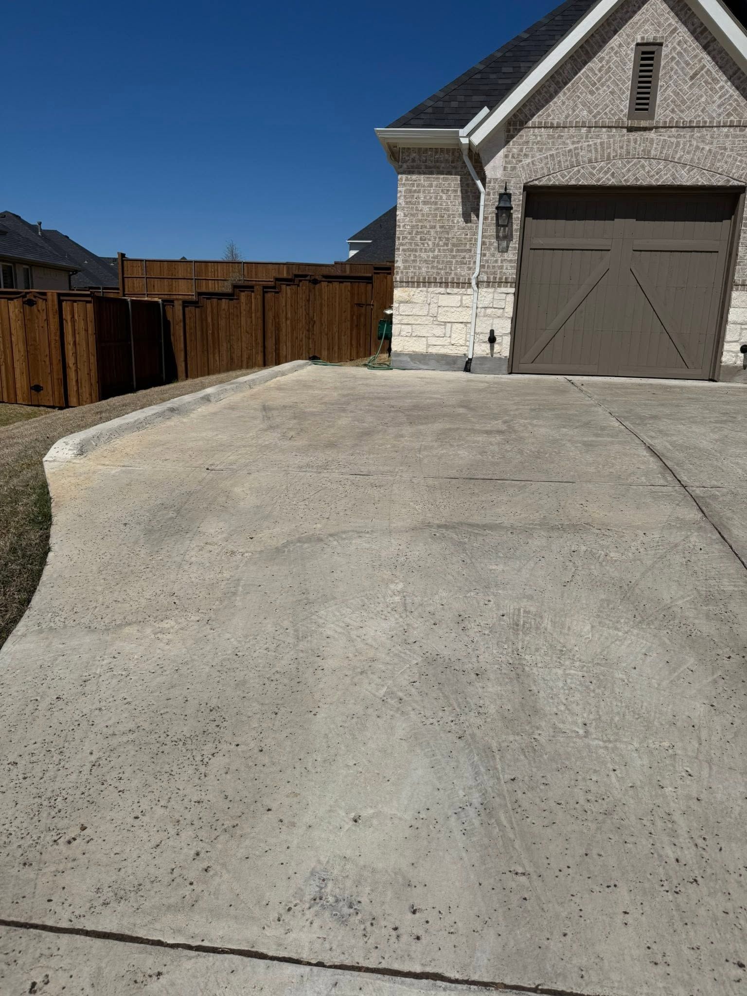 Driveway leading to a beige garage with a wooden fence under a clear blue sky.