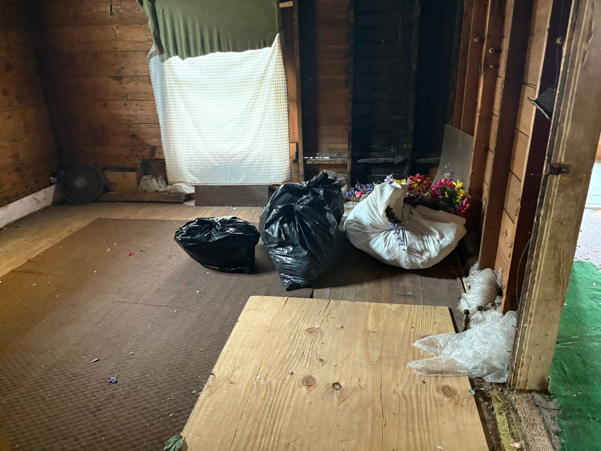 Empty room under renovation with trash bags, a plywood board on the floor, and a covered window.