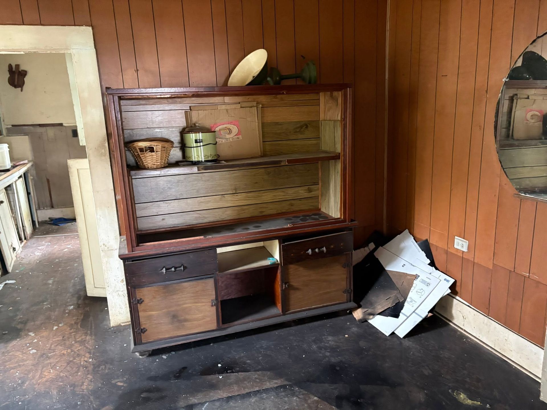 Abandoned room with a wooden hutch, peeling walls, and debris on the floor.