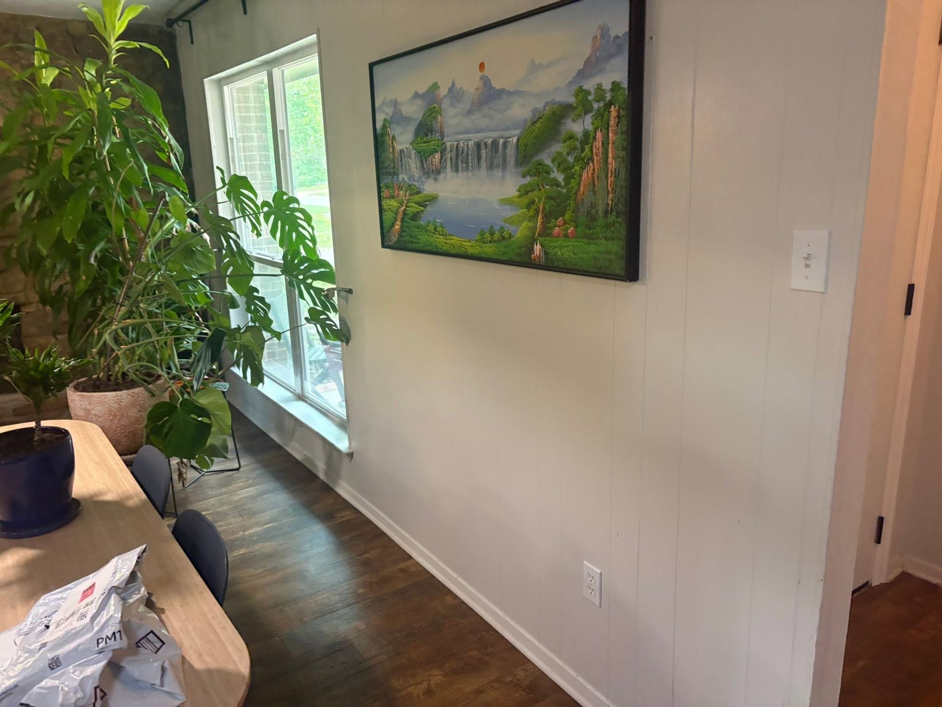 Bright hallway with a window, potted plants, a framed landscape, and a desk with papers in the foreground