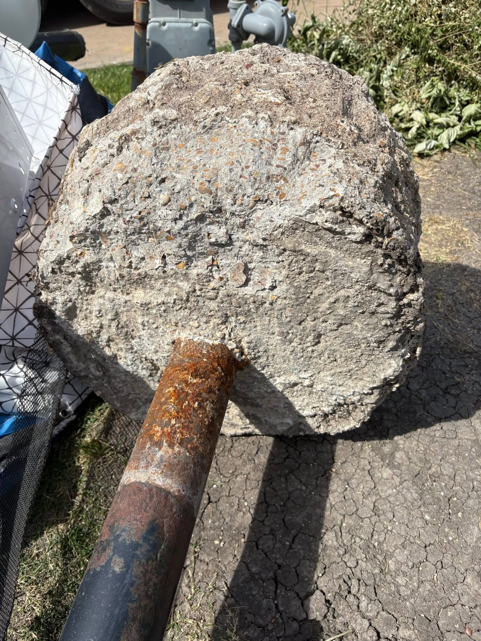 Rusty sledgehammer with a large gray, chipped head on pavement near a chain-link fence.