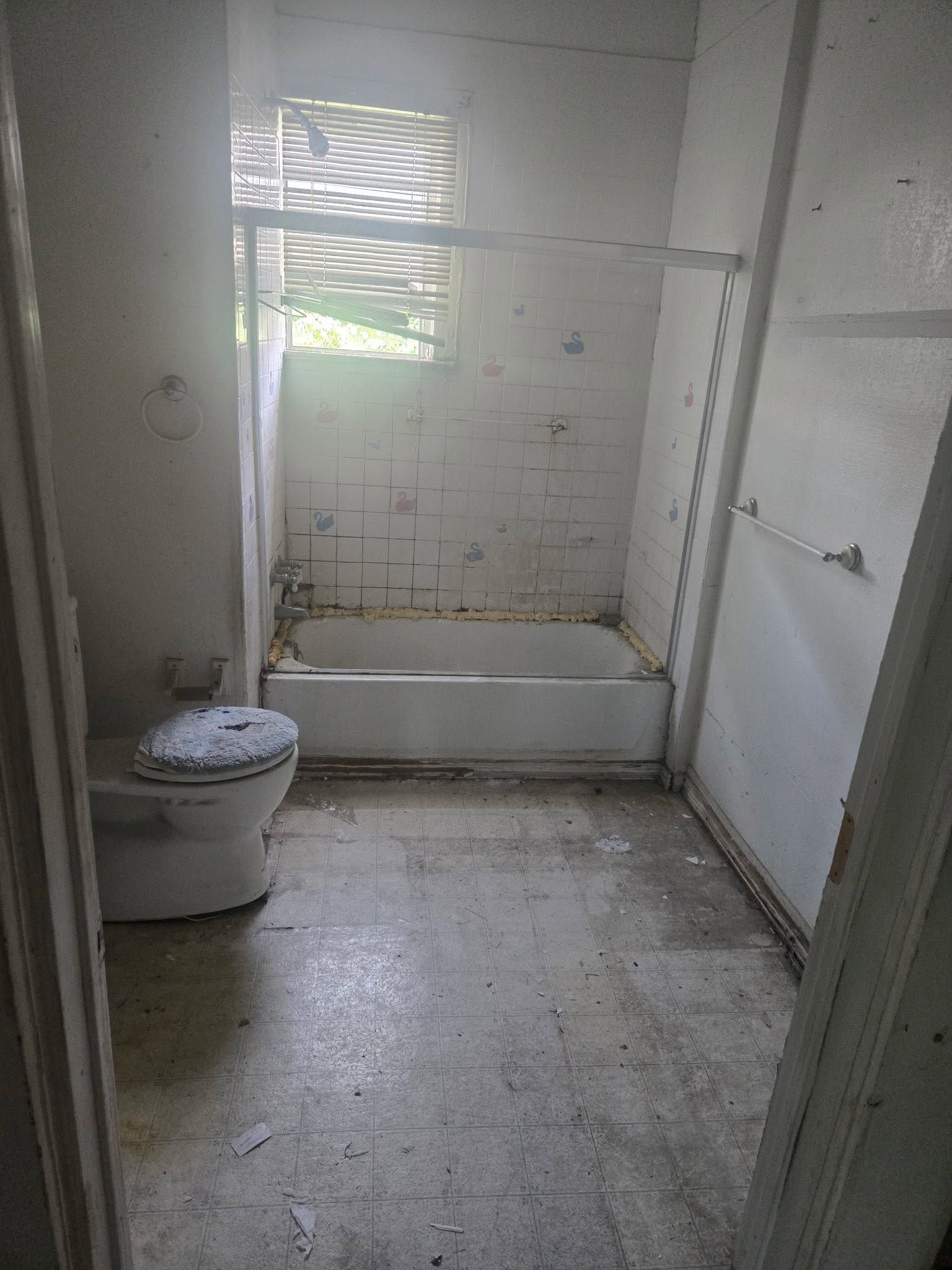 Empty white bathroom with toilet, shower stall, and window with blinds.