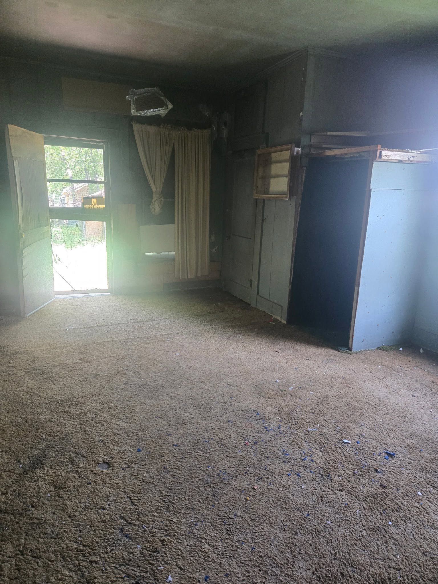 Empty, dimly lit room with a gravel floor, window light, and a blue cabinet against the wall