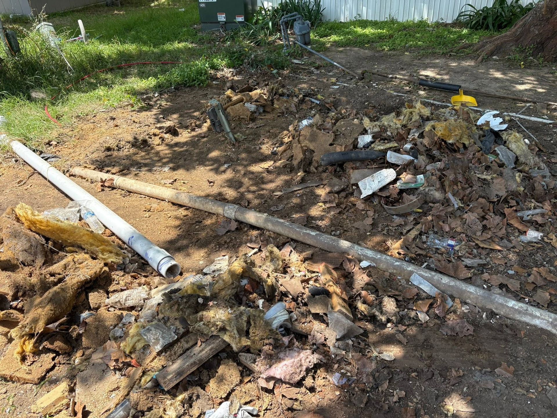 Debris and broken boards scattered on bare ground beside a white pipe in a yard