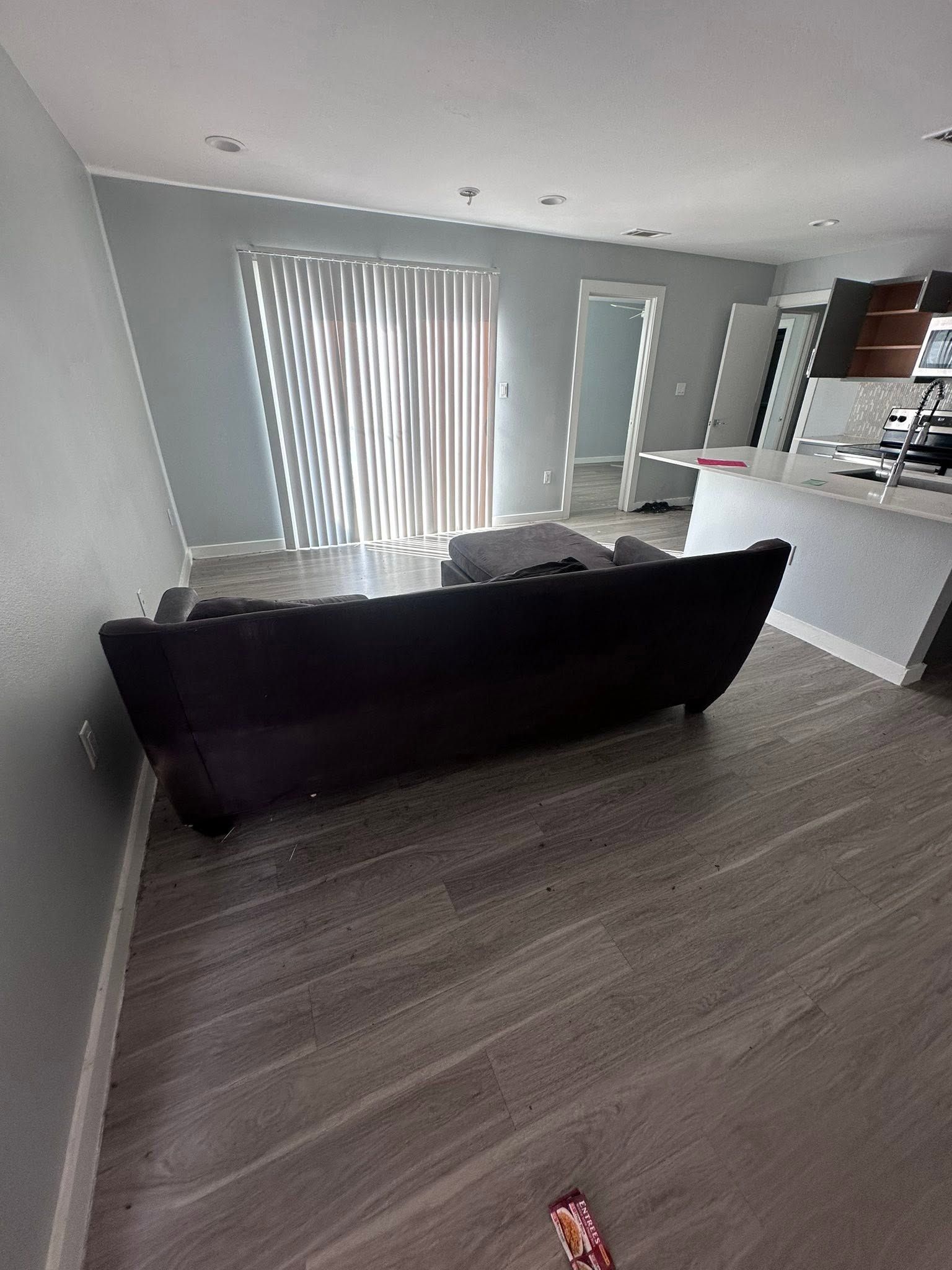 Modern living room with black sofa, gray wood floor, and sliding glass door with vertical blinds.