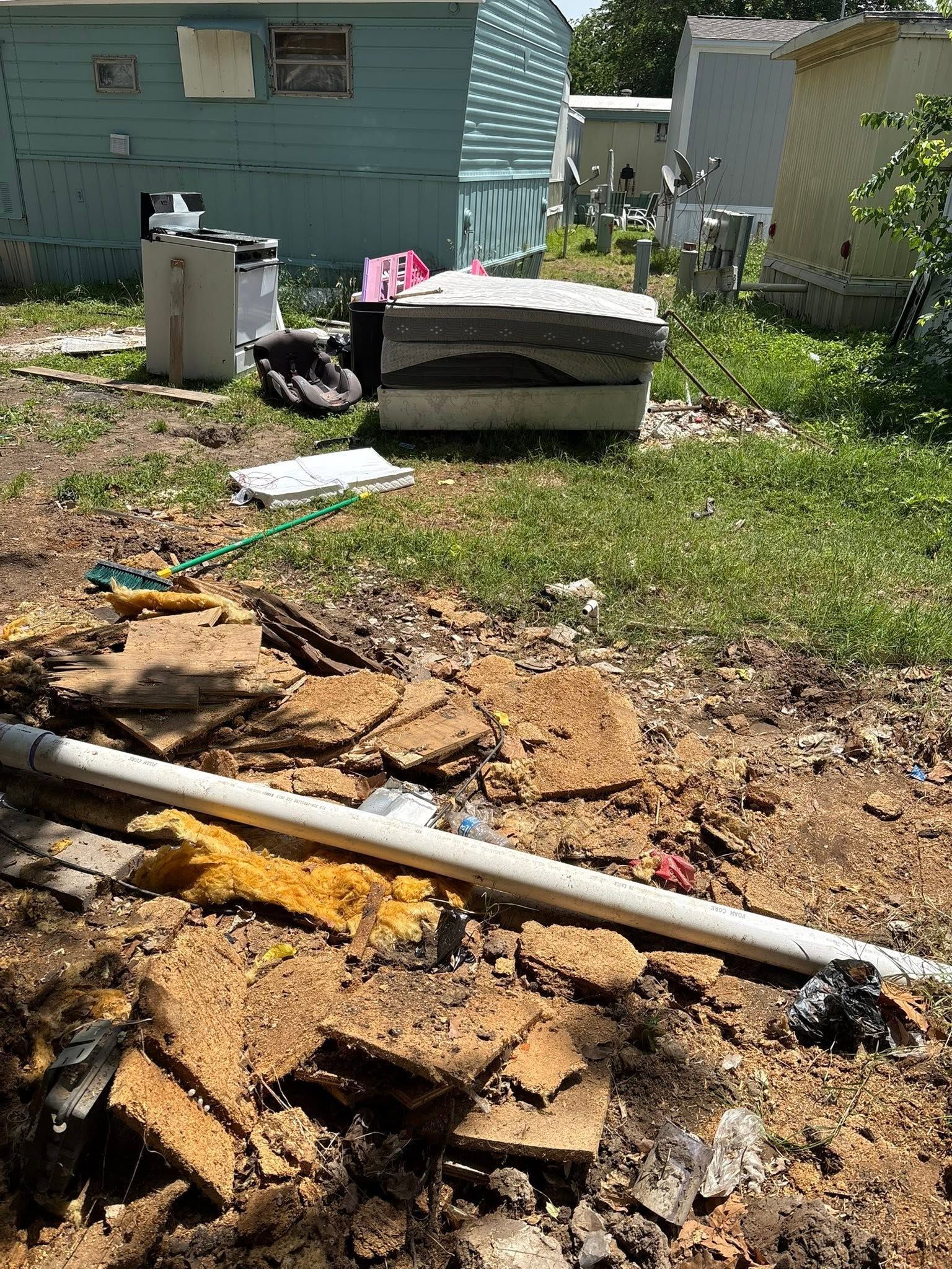 Backyard with torn-up ground, exposed soil, debris, and an old mattress near a house