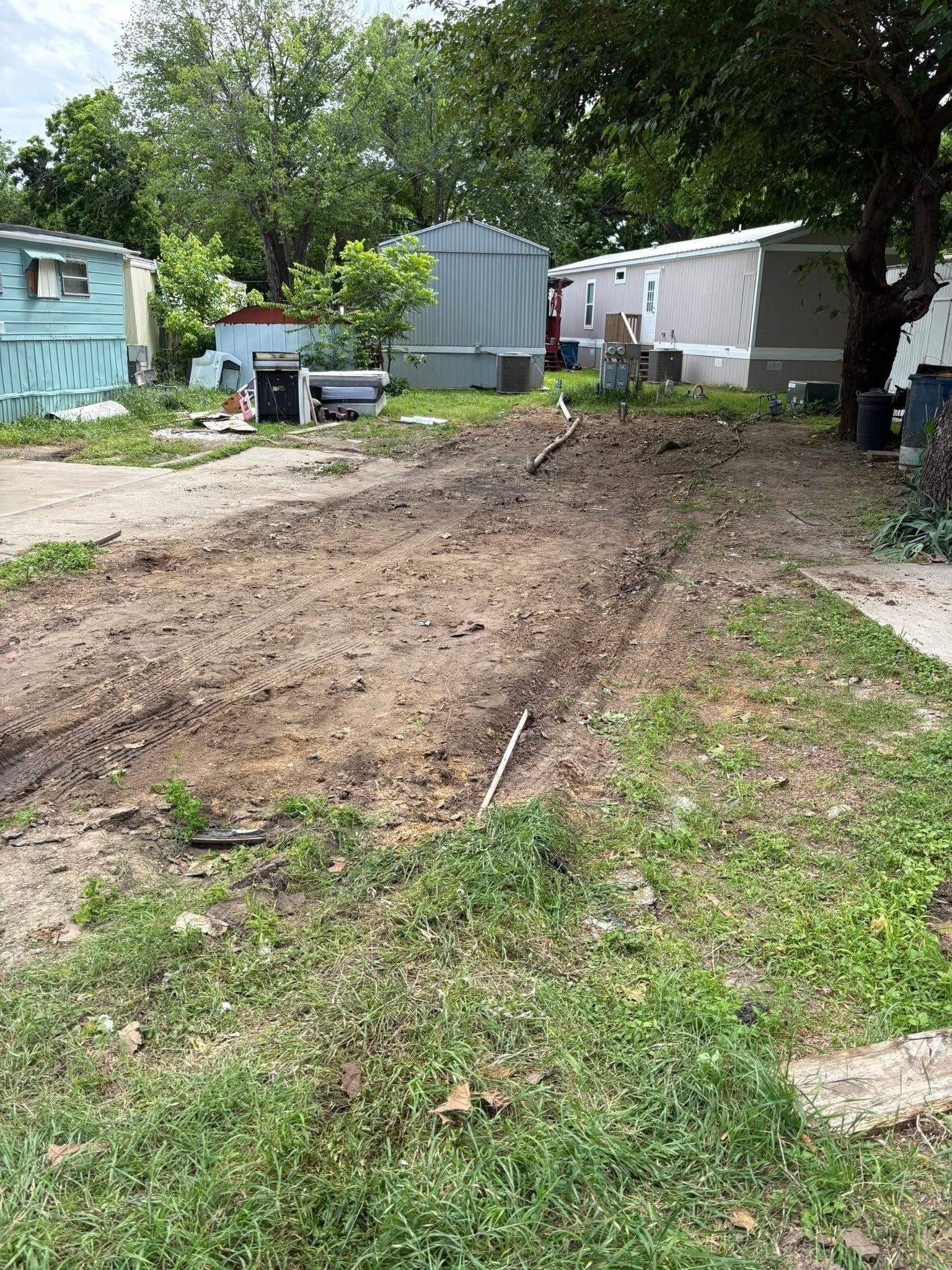 Backyard with a freshly dug dirt trench between mobile homes and trees