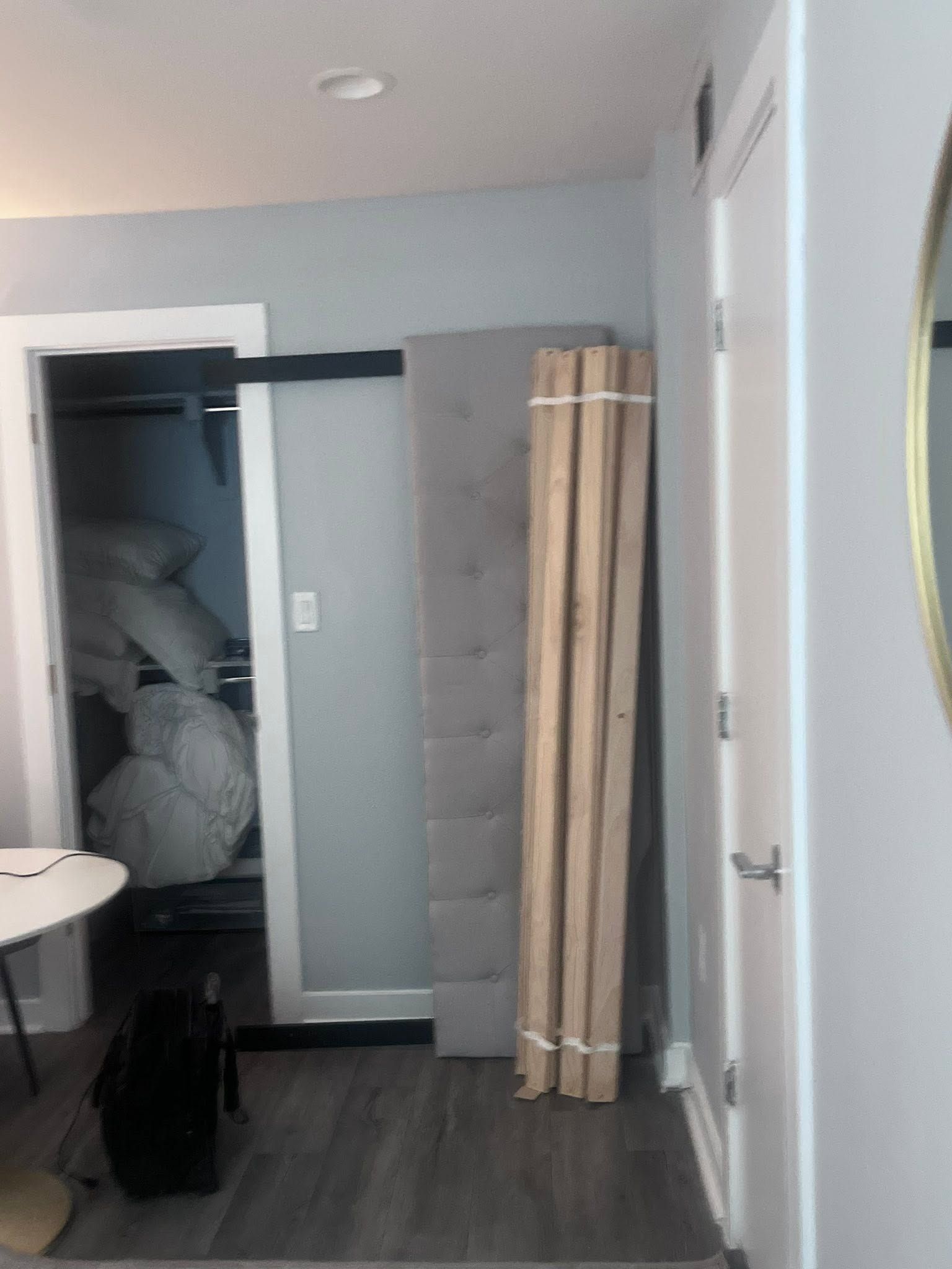 Small room with open closet, white door, gray wall panel, and stacked wooden boards against the wall
