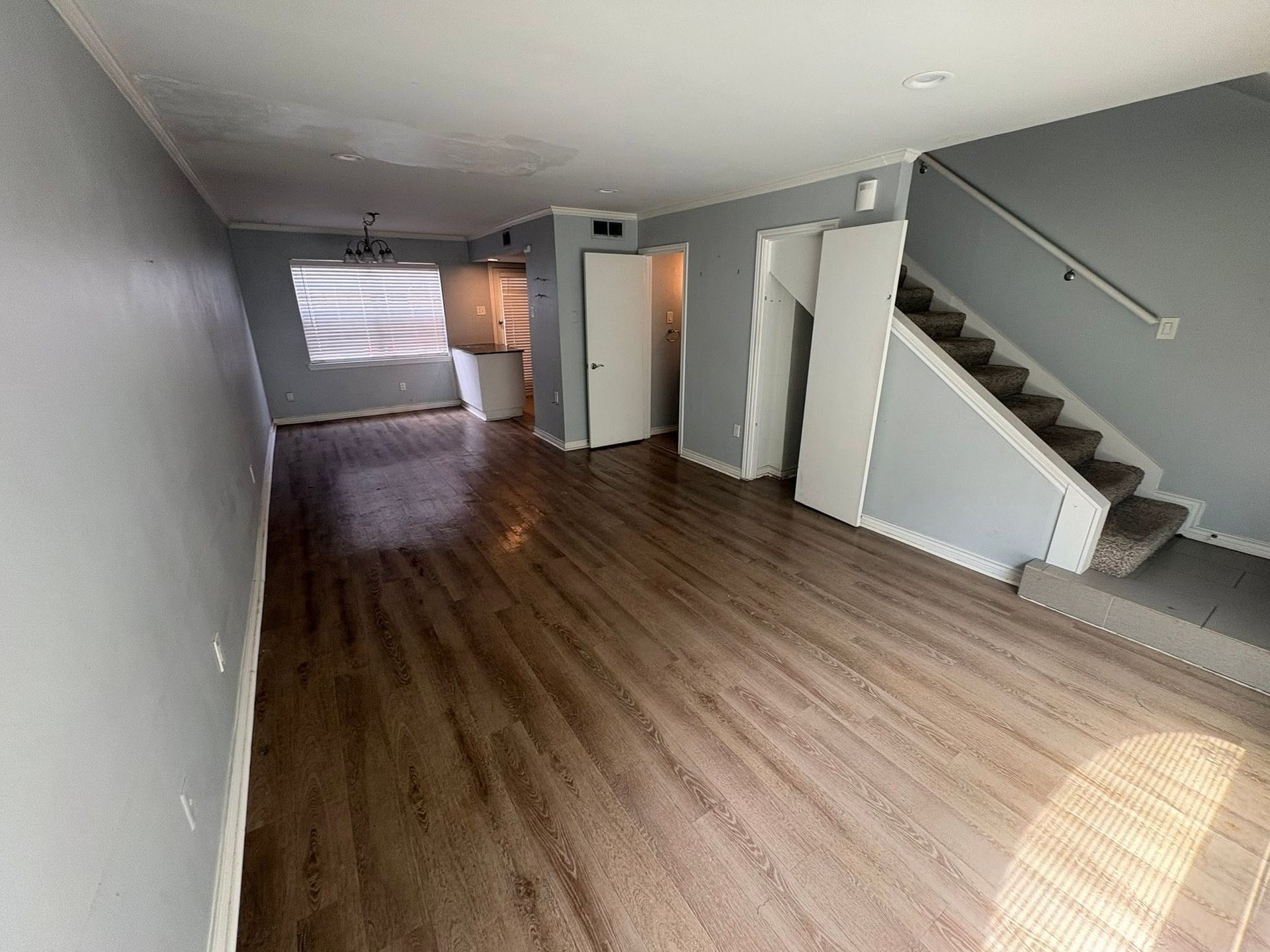 Empty living room with wood floors, gray walls, staircase, and bright window blinds