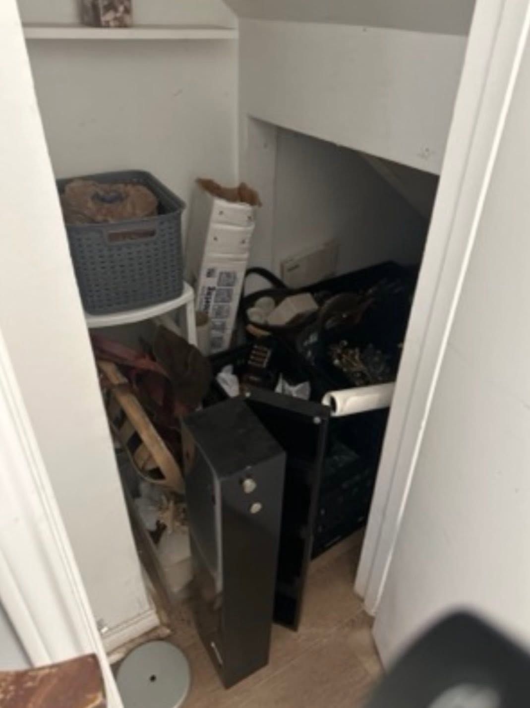 Cluttered closet with boxes, a fan, and assorted items piled on the floor