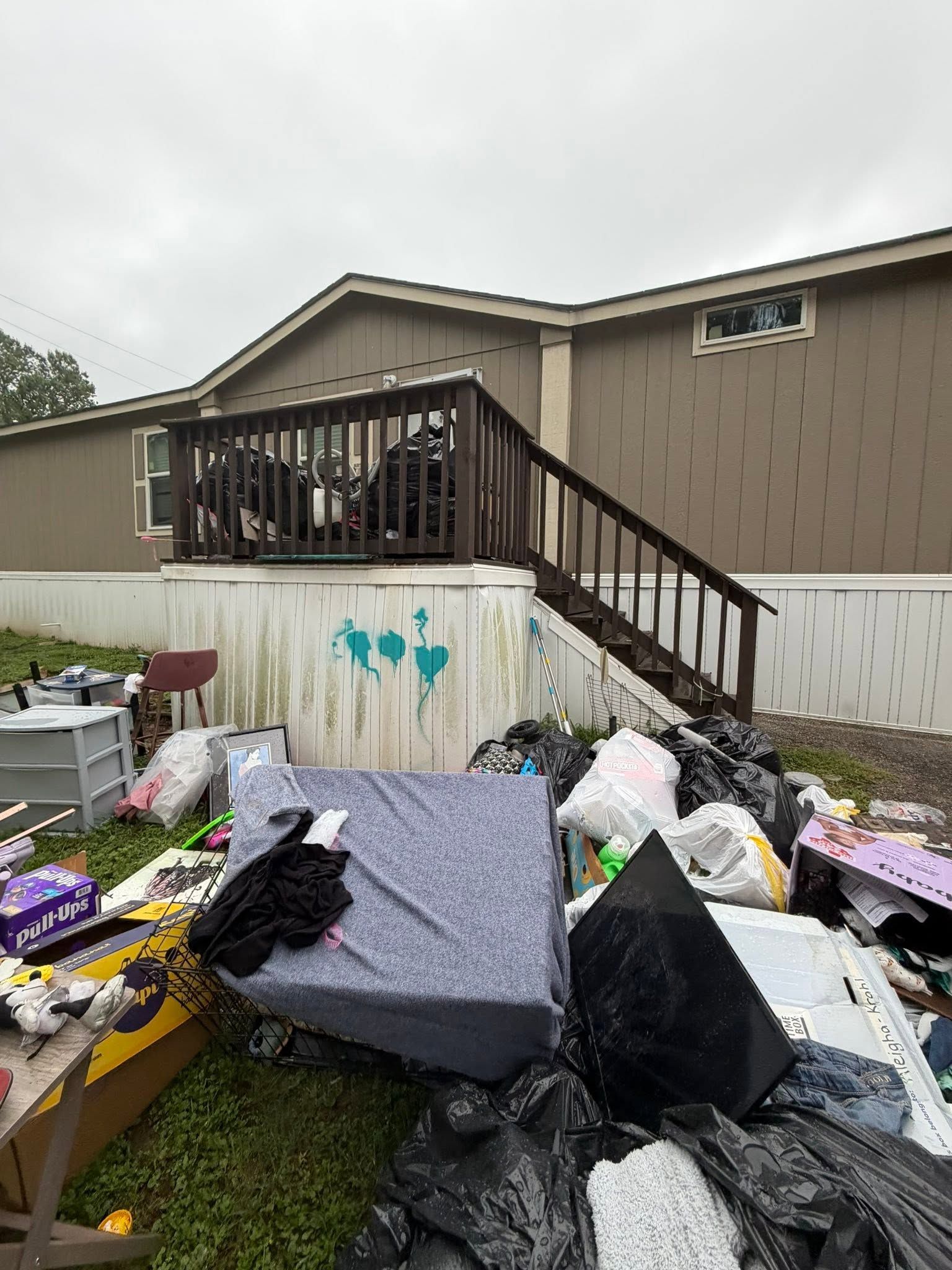 Flood damage with scattered debris and trash piled outside a beige mobile home.