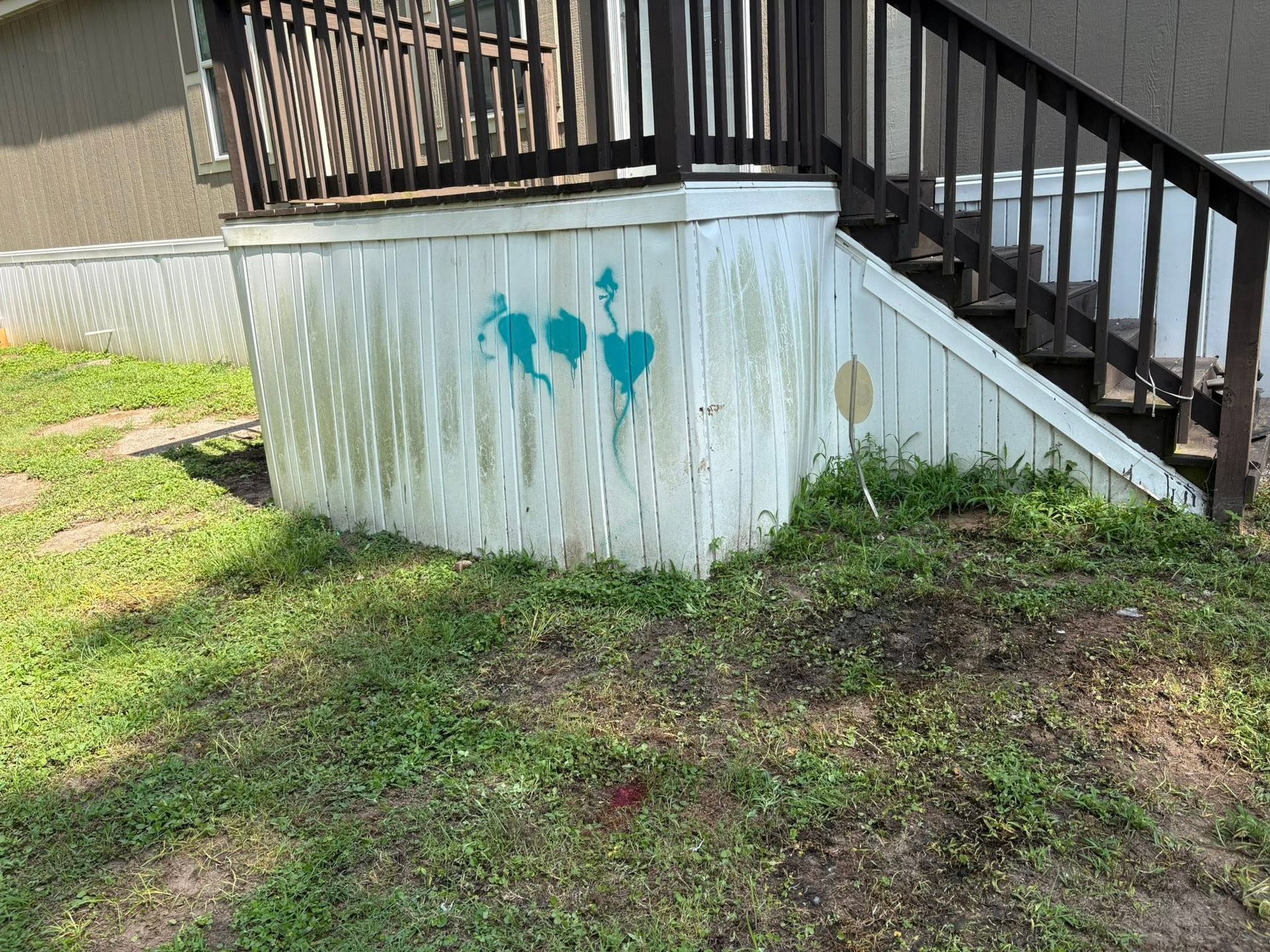 Wooden porch stairs beside a white skirting wall with teal paint marks over patchy grass and dirt.