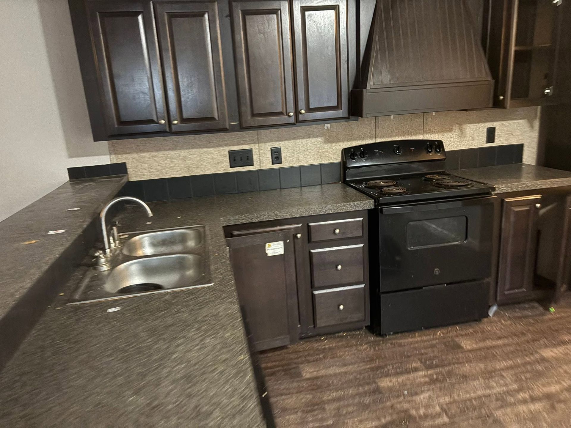 Dark kitchen with black cabinets, granite countertops, stainless sink, and black stove.