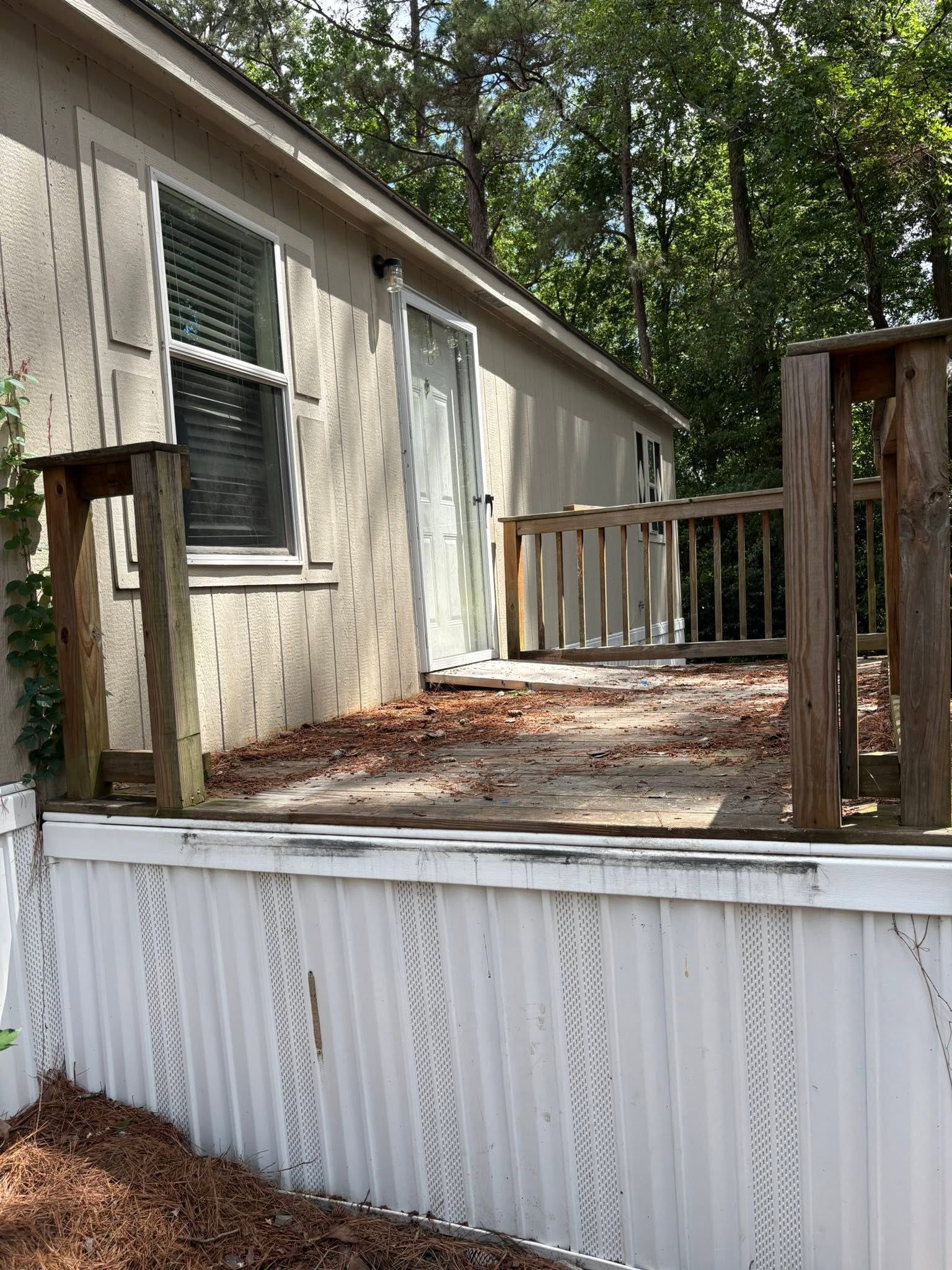Wooden deck beside a white house with railing and trees in the background.
