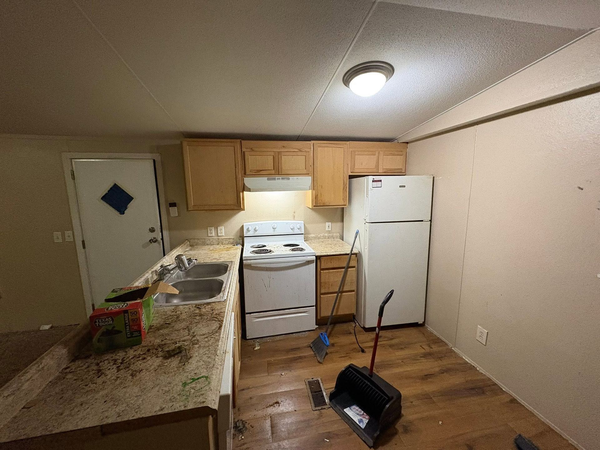 Small kitchen with white appliances, wood cabinets, granite counters, and a cleaning mop on the floor.