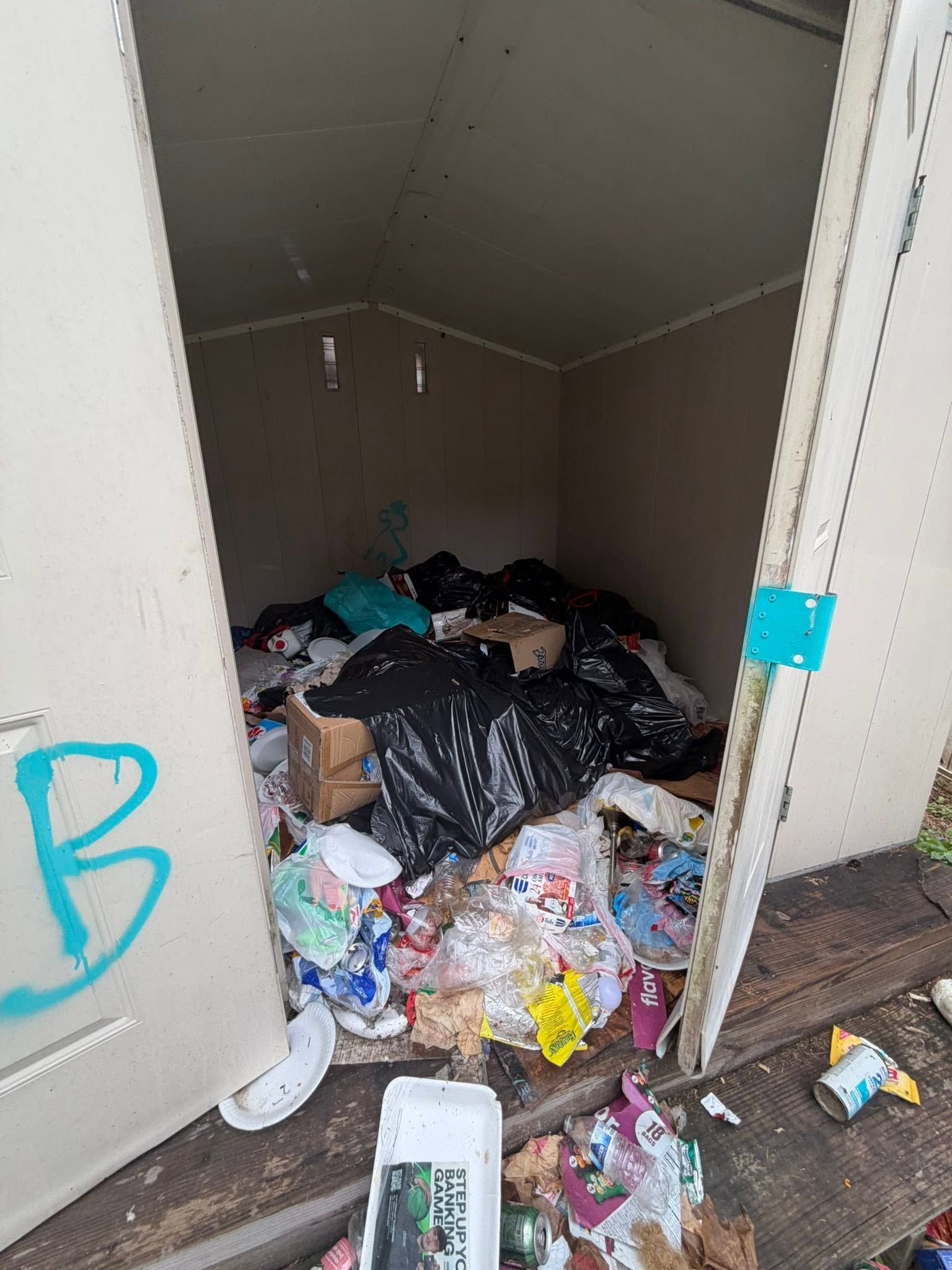 Overflowing trash piled inside a small beige utility room with an open door.