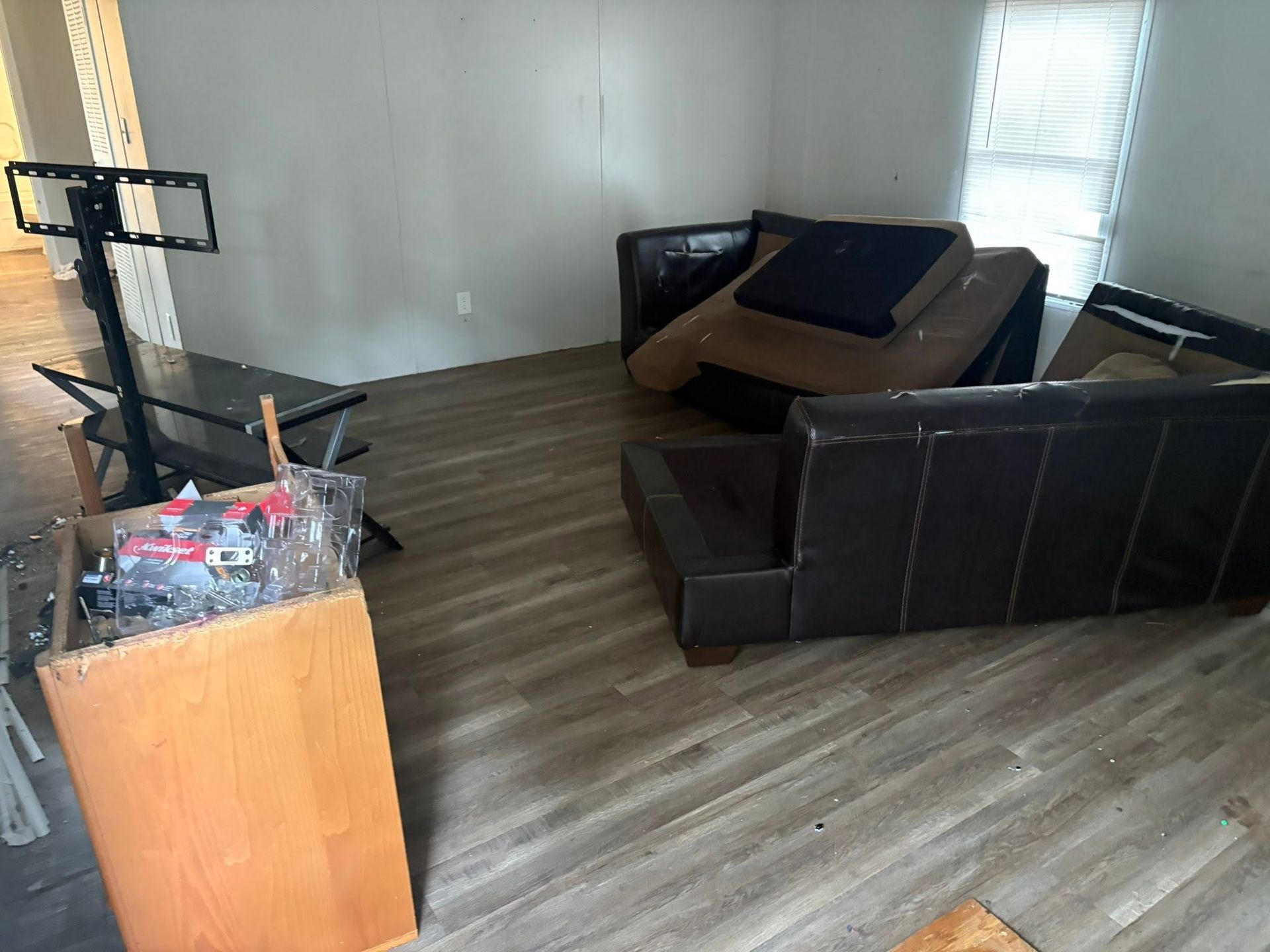 Cluttered living room with a tipped couch, broken furniture, and a TV stand against bare walls.