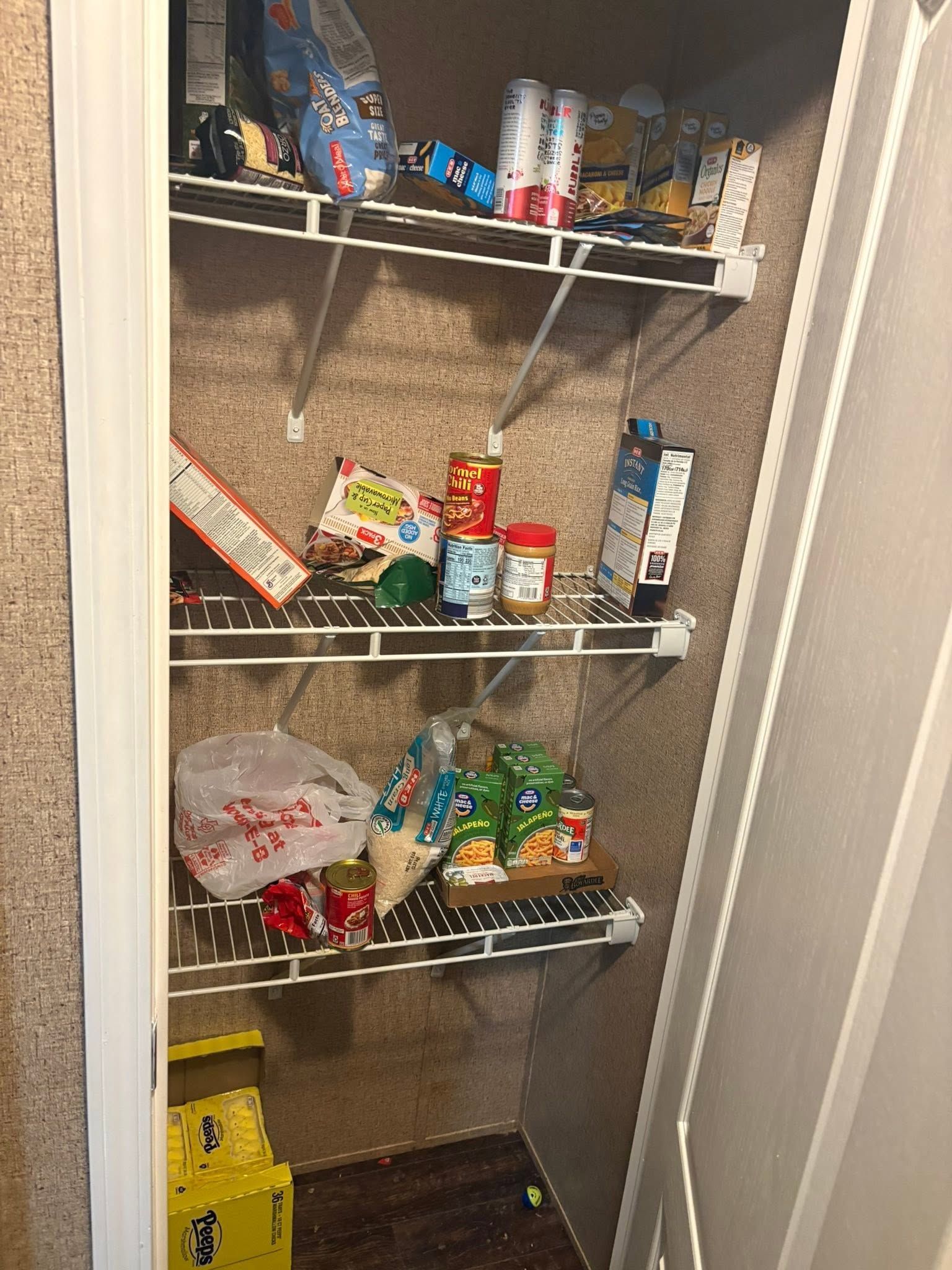 Open pantry closet with wire shelves holding assorted snacks, cans, and household items.