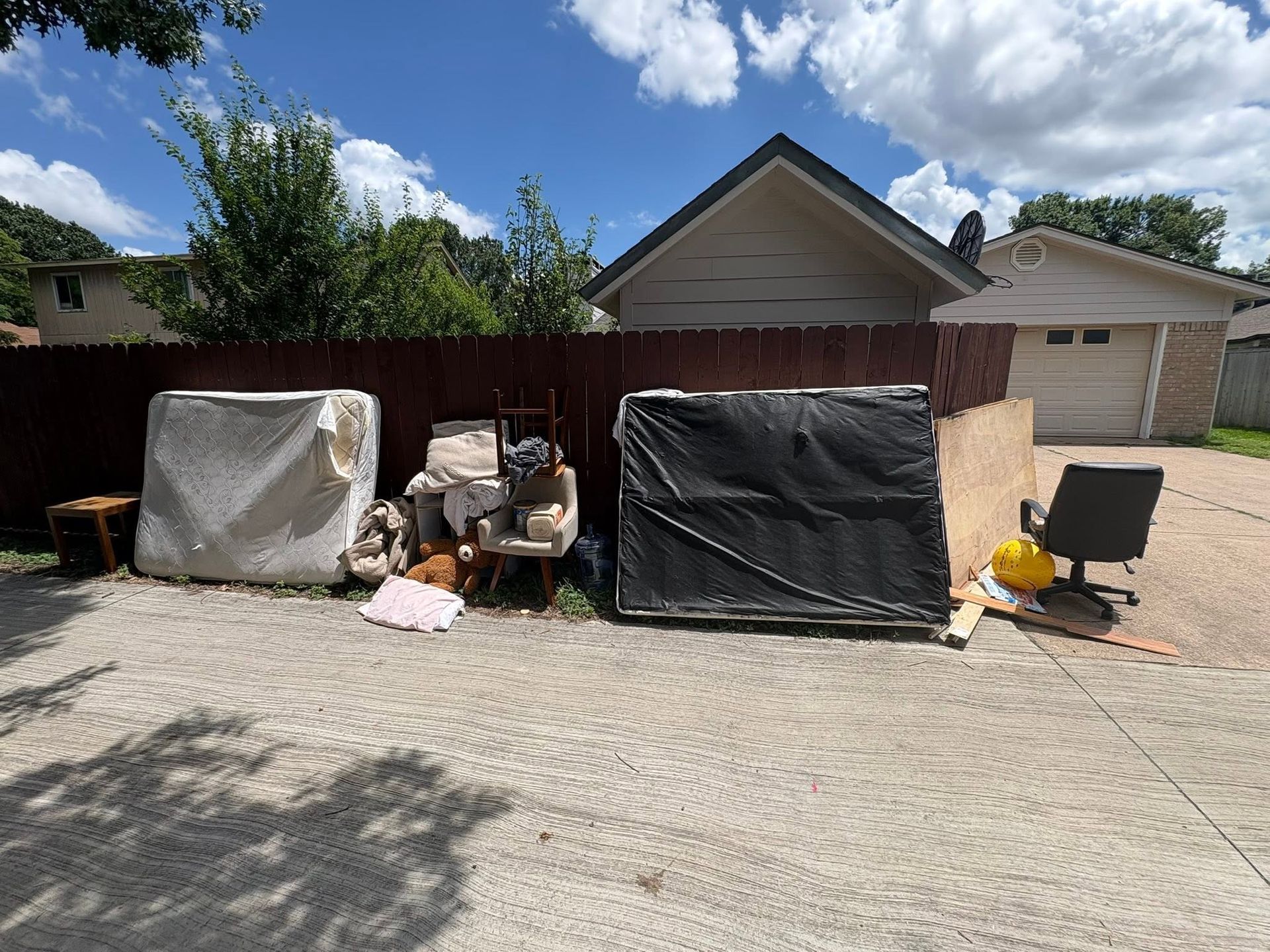 Backyard storage items and covered furniture against a wooden fence on a sunny day