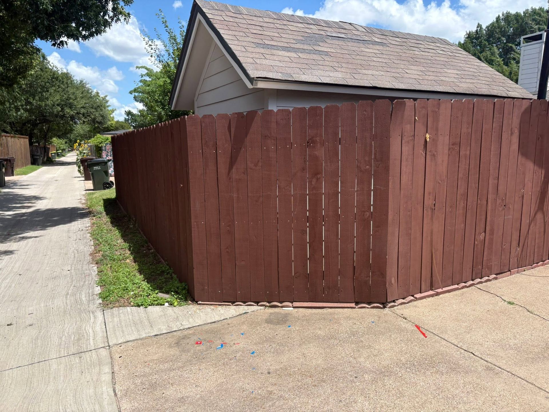 Brown wooden fence beside a house along a narrow driveway on a sunny day