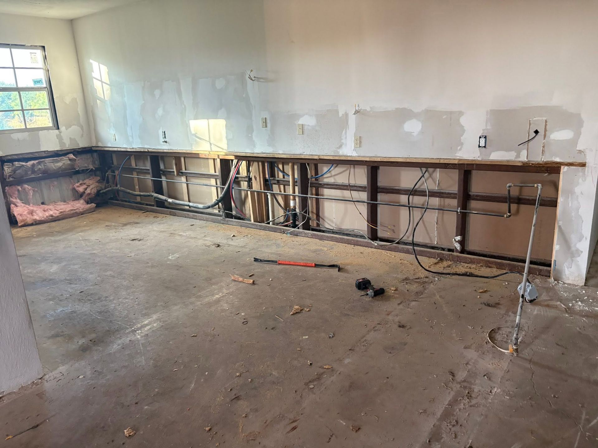 Empty room under renovation with unfinished walls, exposed framing, and debris on the floor
