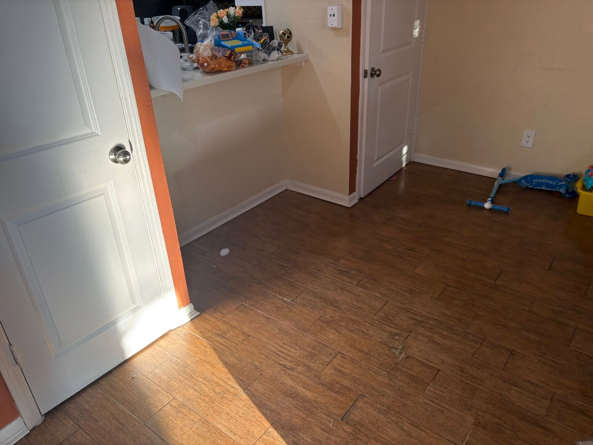 Empty room with wood floor, beige walls, white doors, and a small wall shelf with items.
