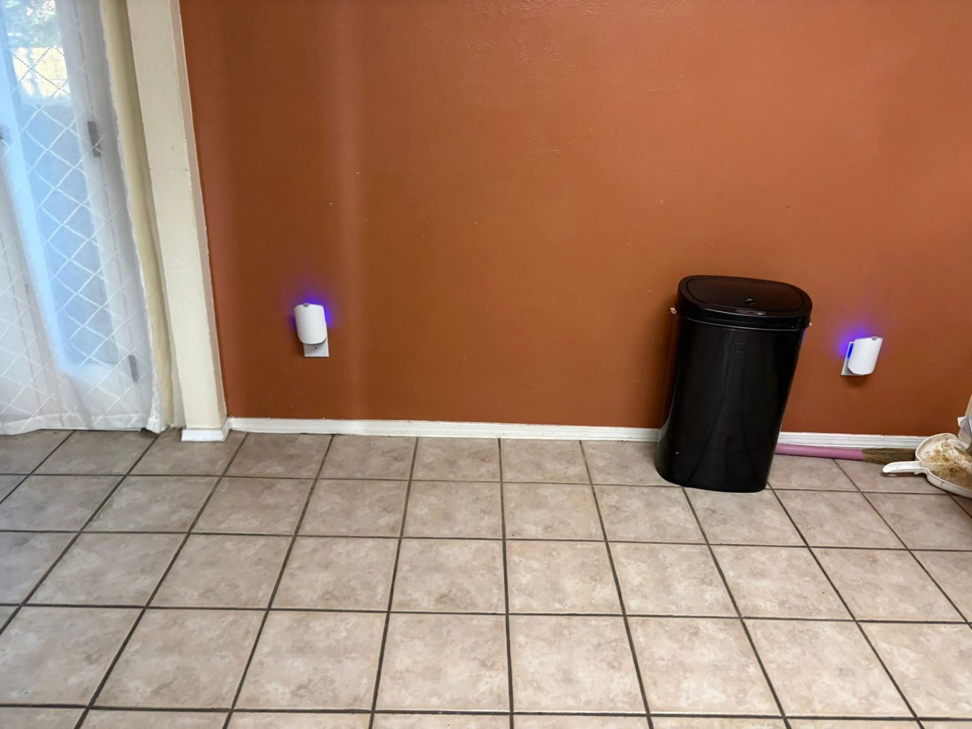Empty tiled room with orange wall, two purple wall lights, and a black trash can in the corner