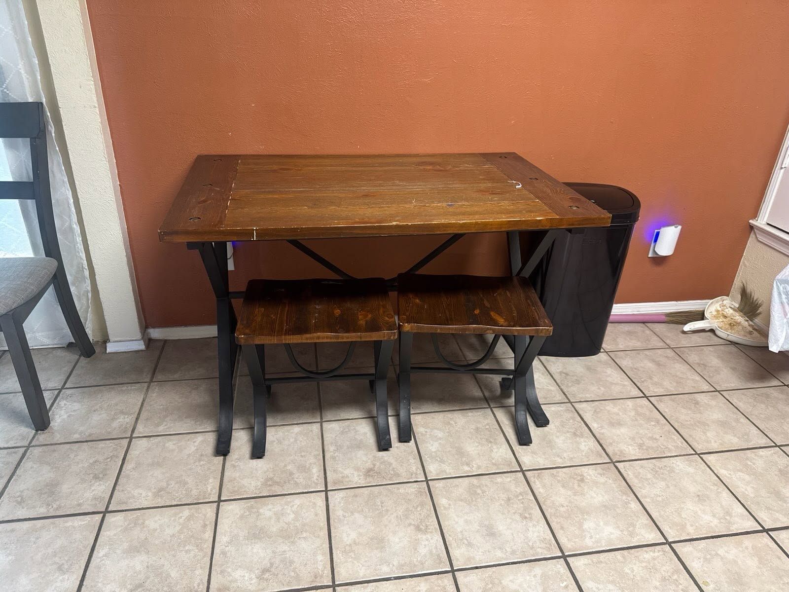 Small wooden table with two benches against an orange wall on a tiled floor