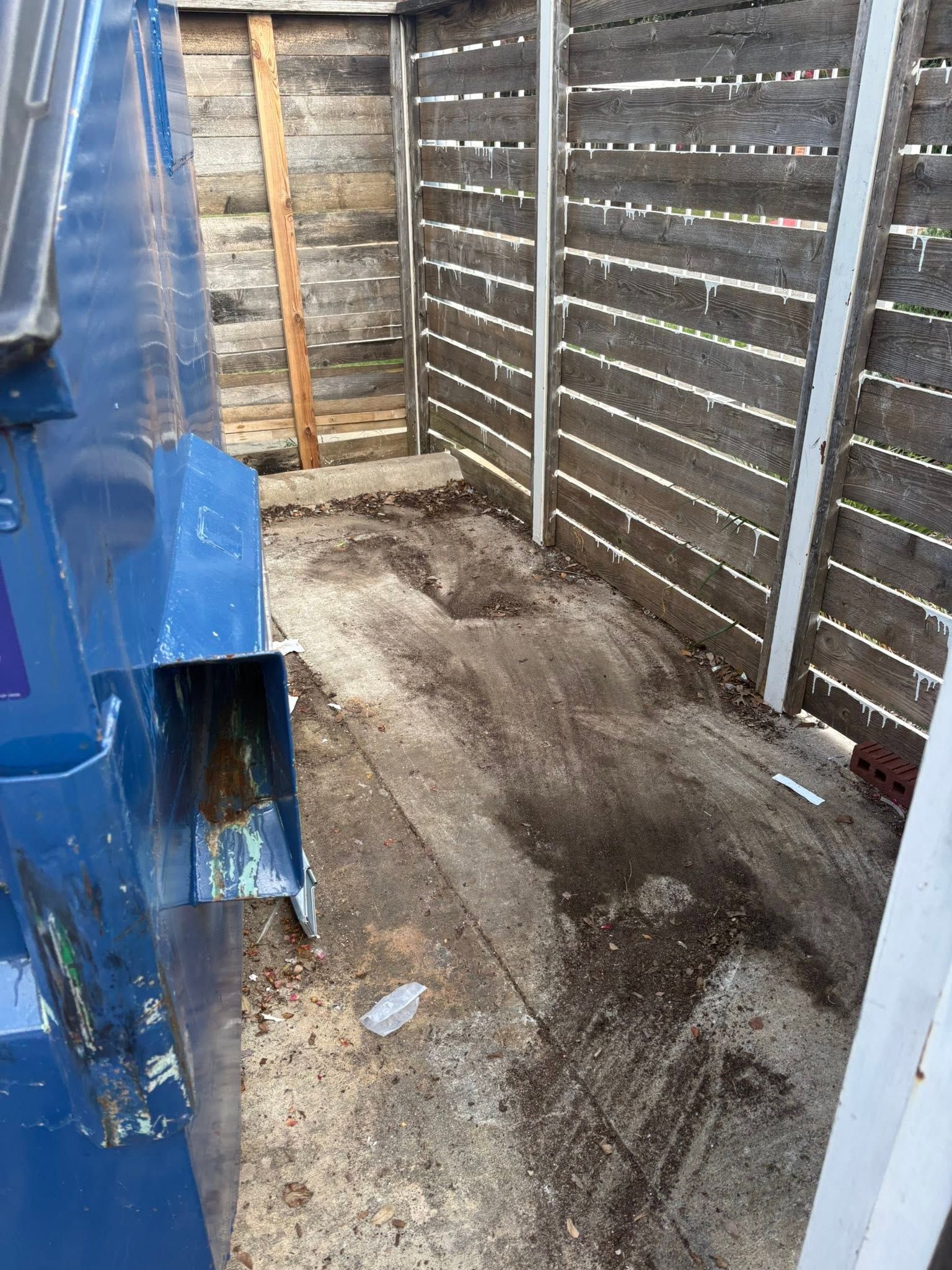 Narrow dirt alley between weathered wooden fences with a blue metal structure on the left.