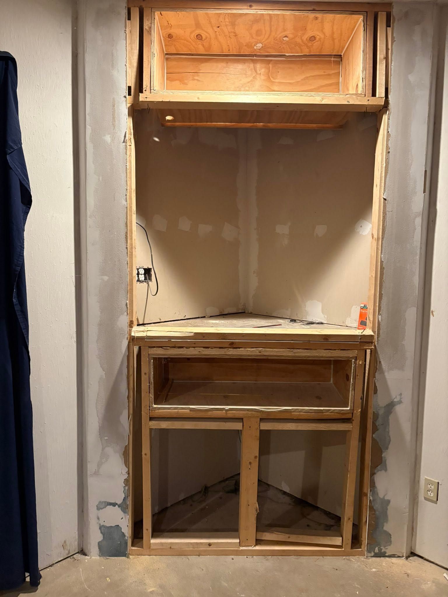 Built-in wall cabinet opening under construction, with exposed wood framing and unfinished drywall.