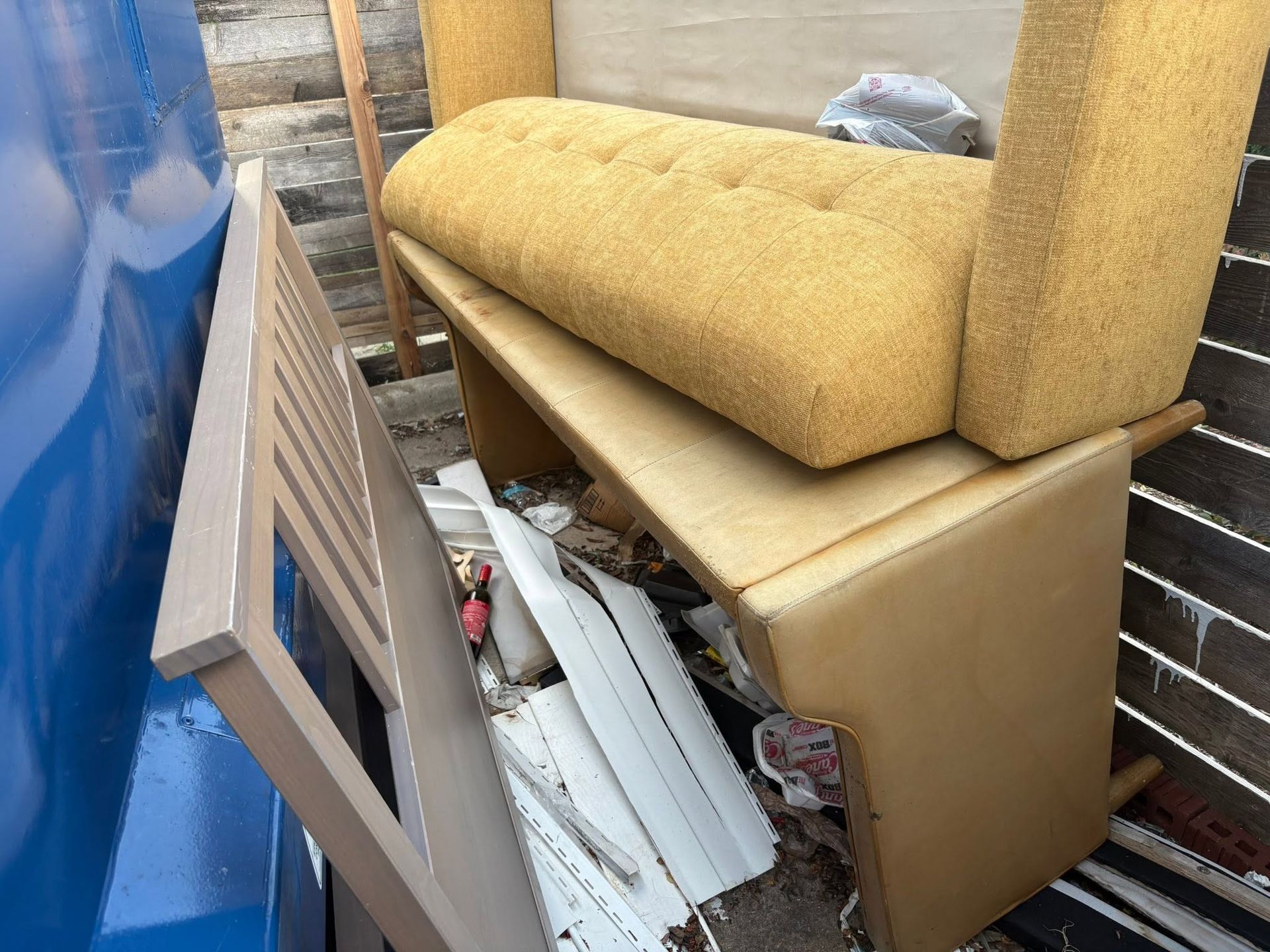 Discarded foam cushions and wood pieces piled in a cramped storage area, with a blue panel on the left.