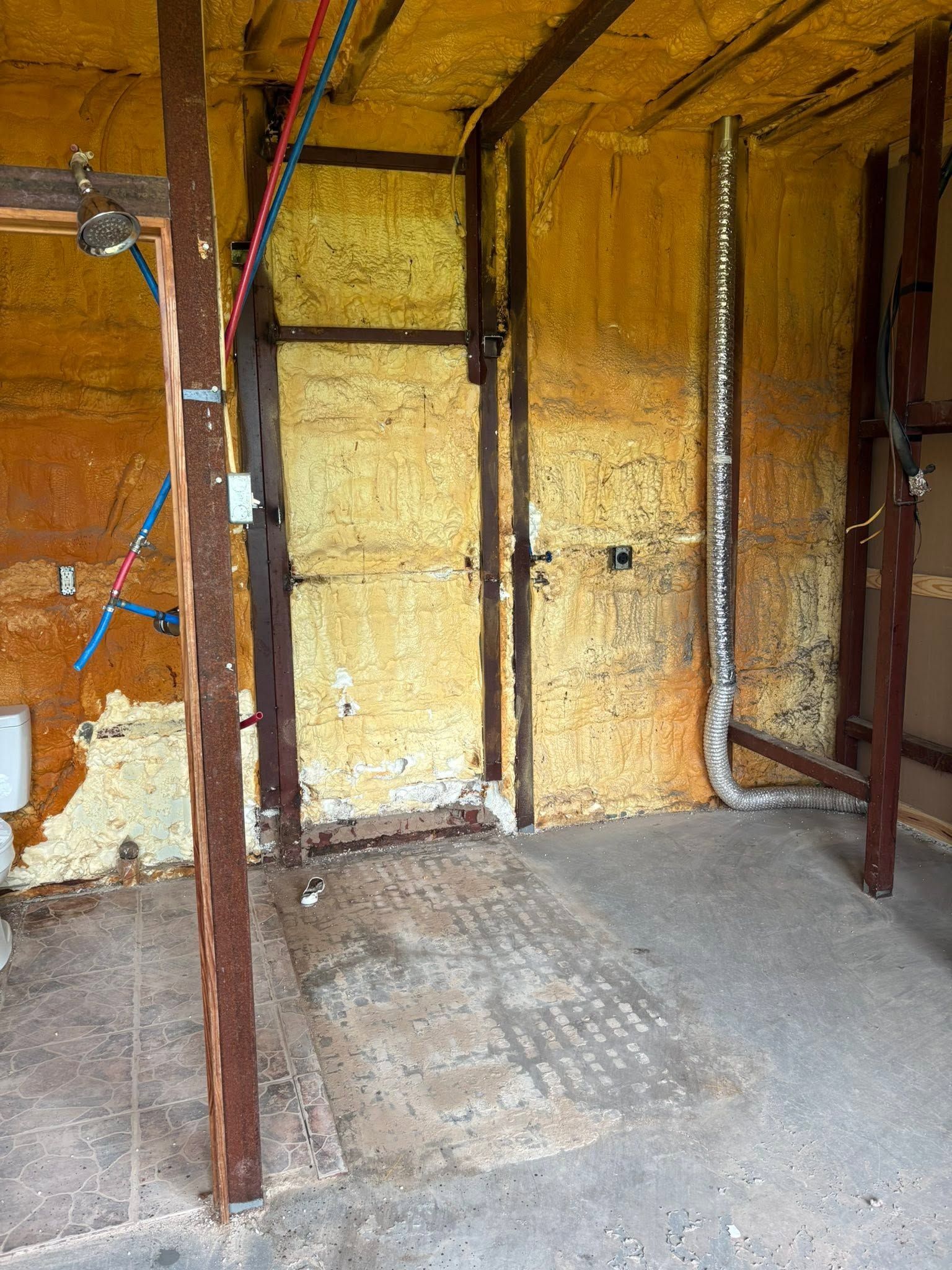 Unfinished room interior with exposed insulation, wooden studs, and a bare concrete floor
