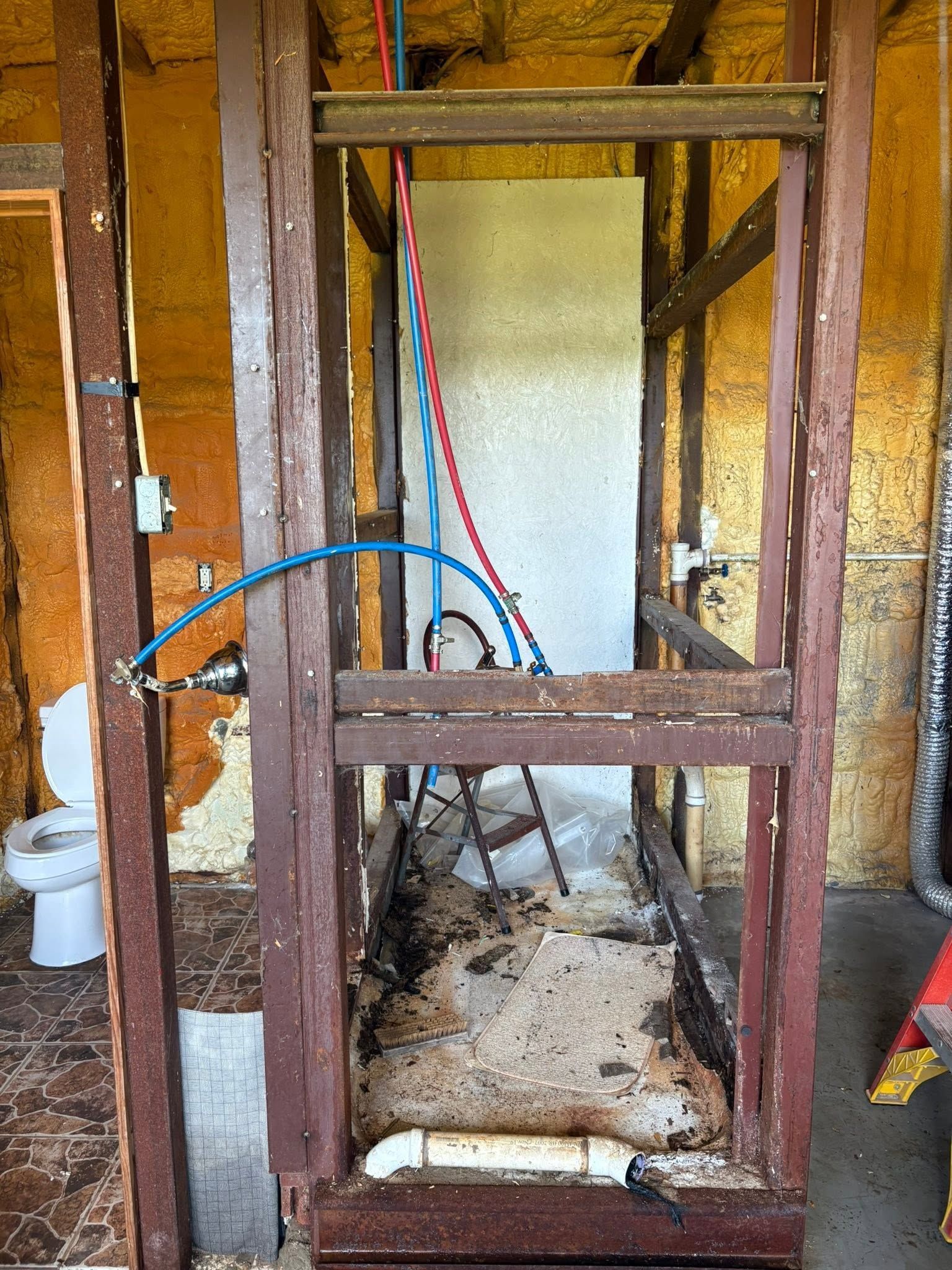 Partially built wooden frame with exposed pipes and wiring in an unfinished room
